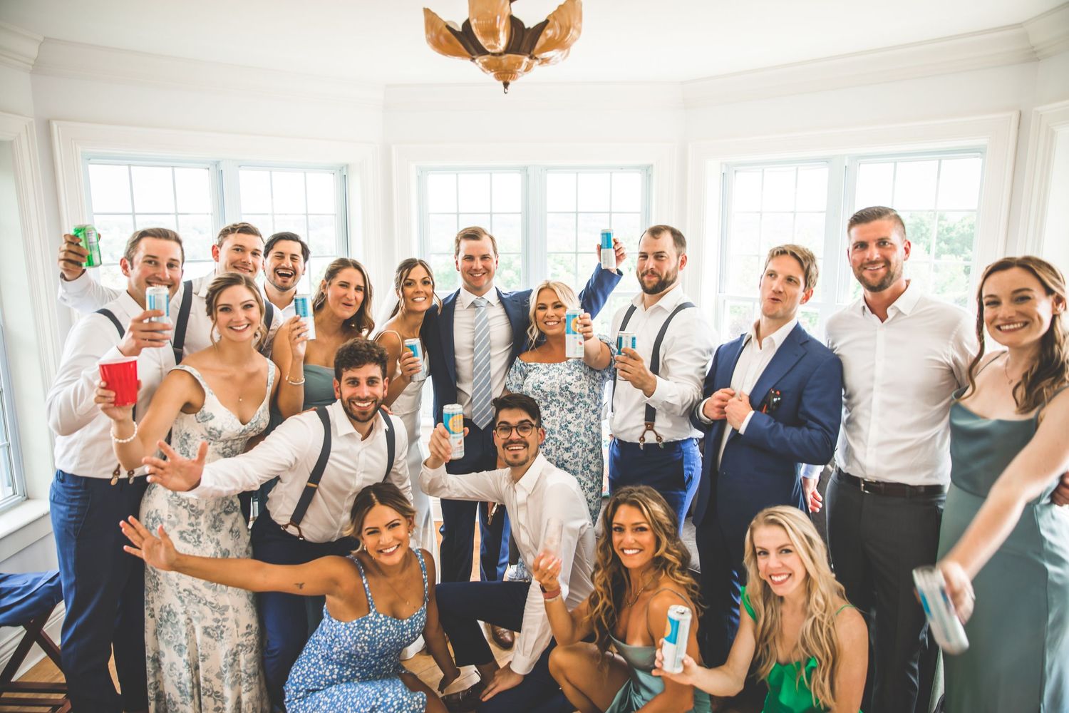 Wedding guests celebrate joyfully in a group photo at an outdoor venue.
