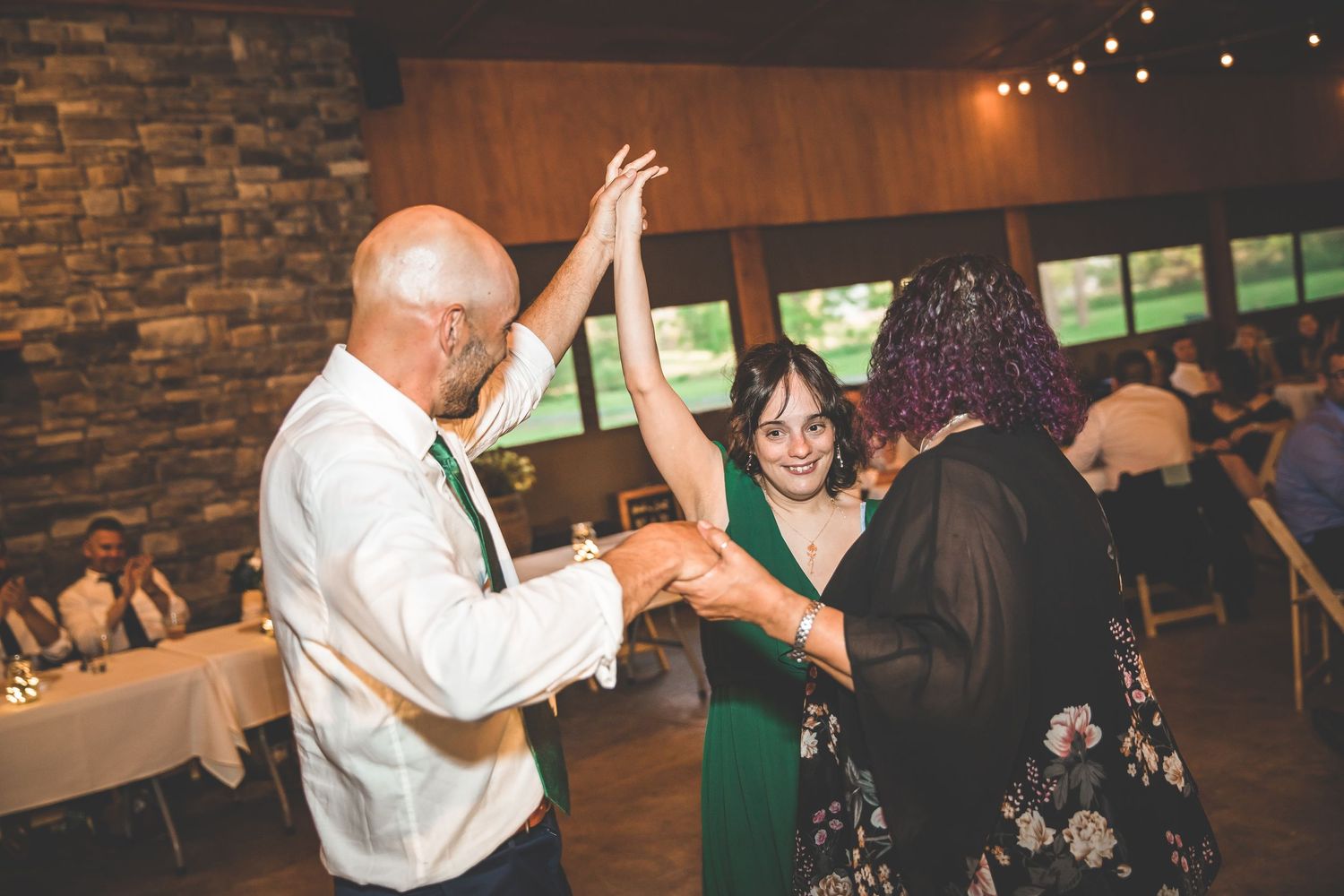 Wedding guests dancing together in a rustic venue with stone walls and string lights.