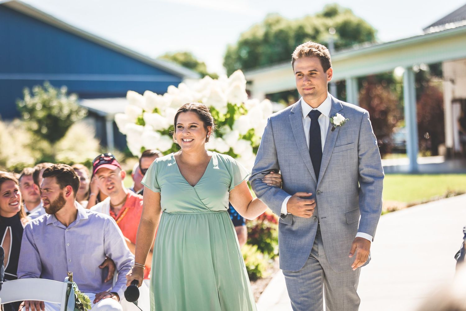 Outdoor wedding processional with attendants walking down the aisle on a sunny day.