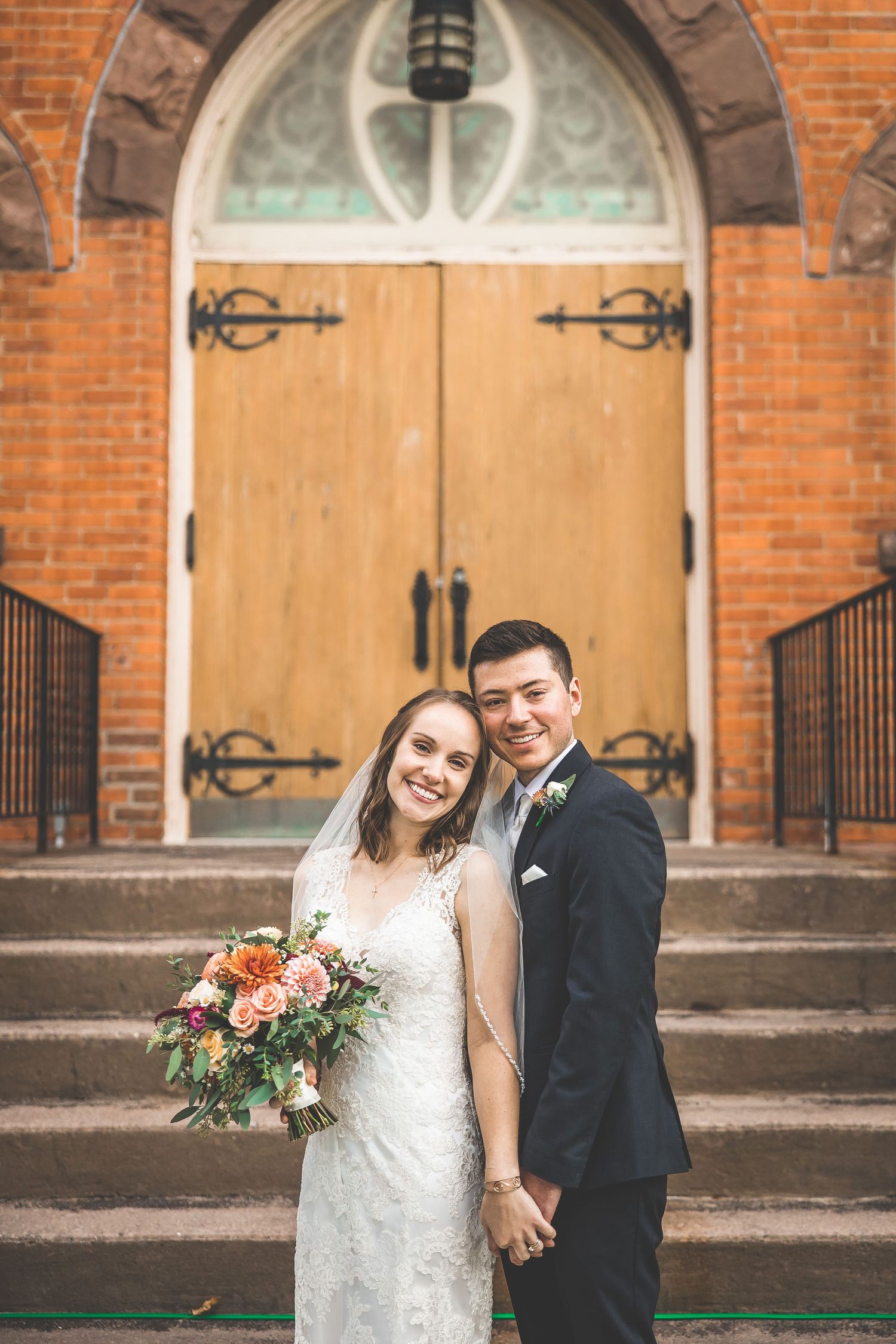 Couple shares happy moments on church steps with red brick facade and wooden doors.
