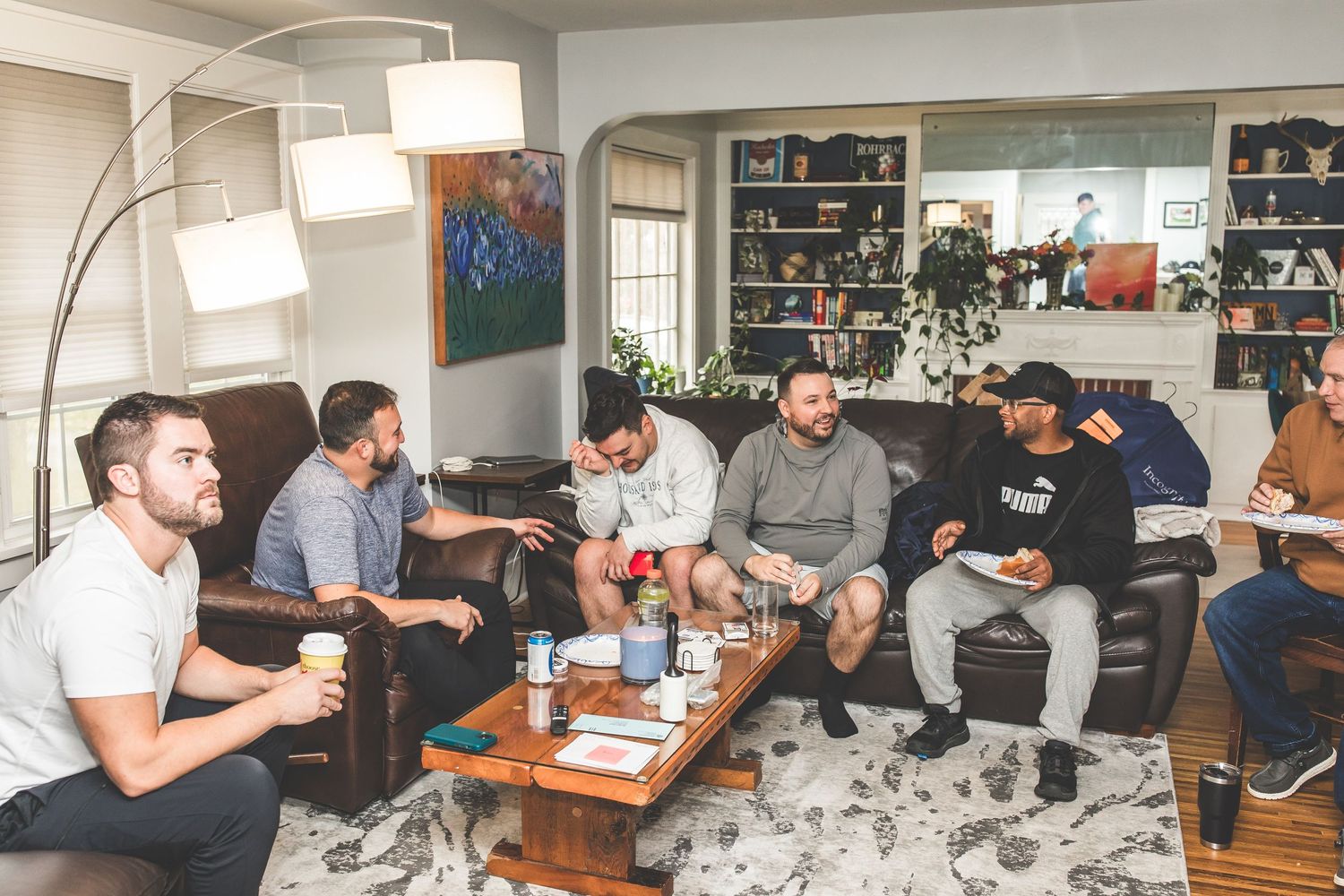 A group gathers in a casual living room setting with modern decor and bookshelves for a relaxed social gathering.