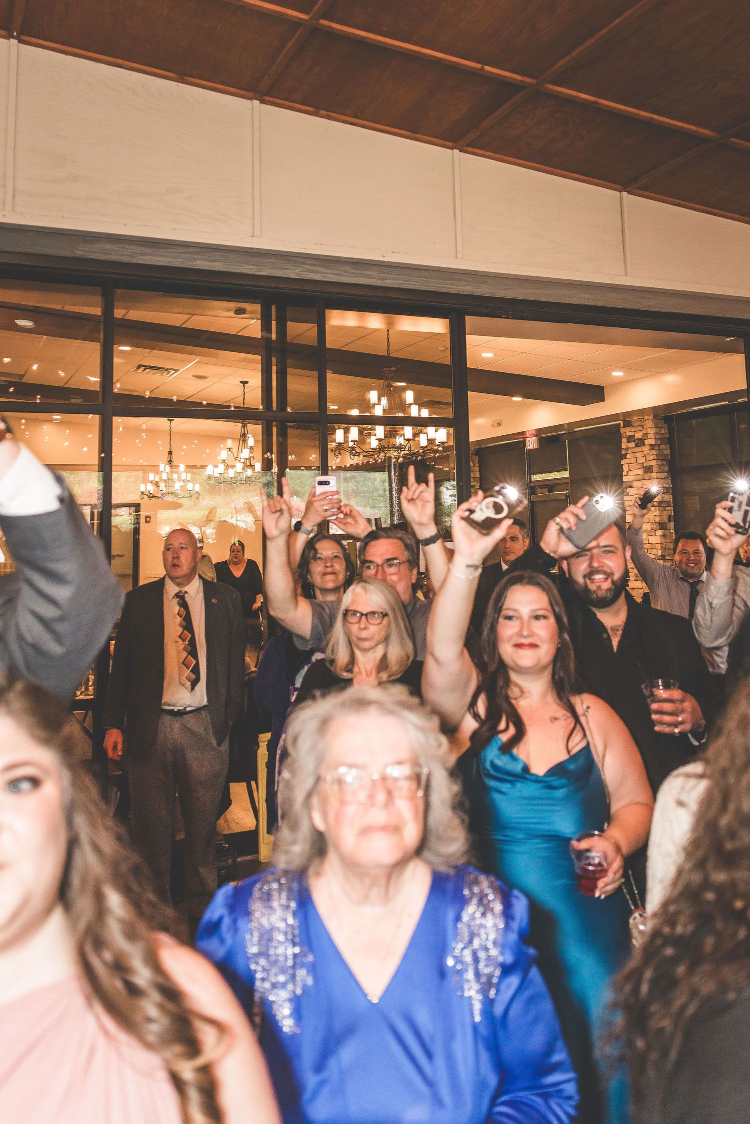 Wedding reception guests celebrating with raised hands and joyful expressions in an indoor venue.