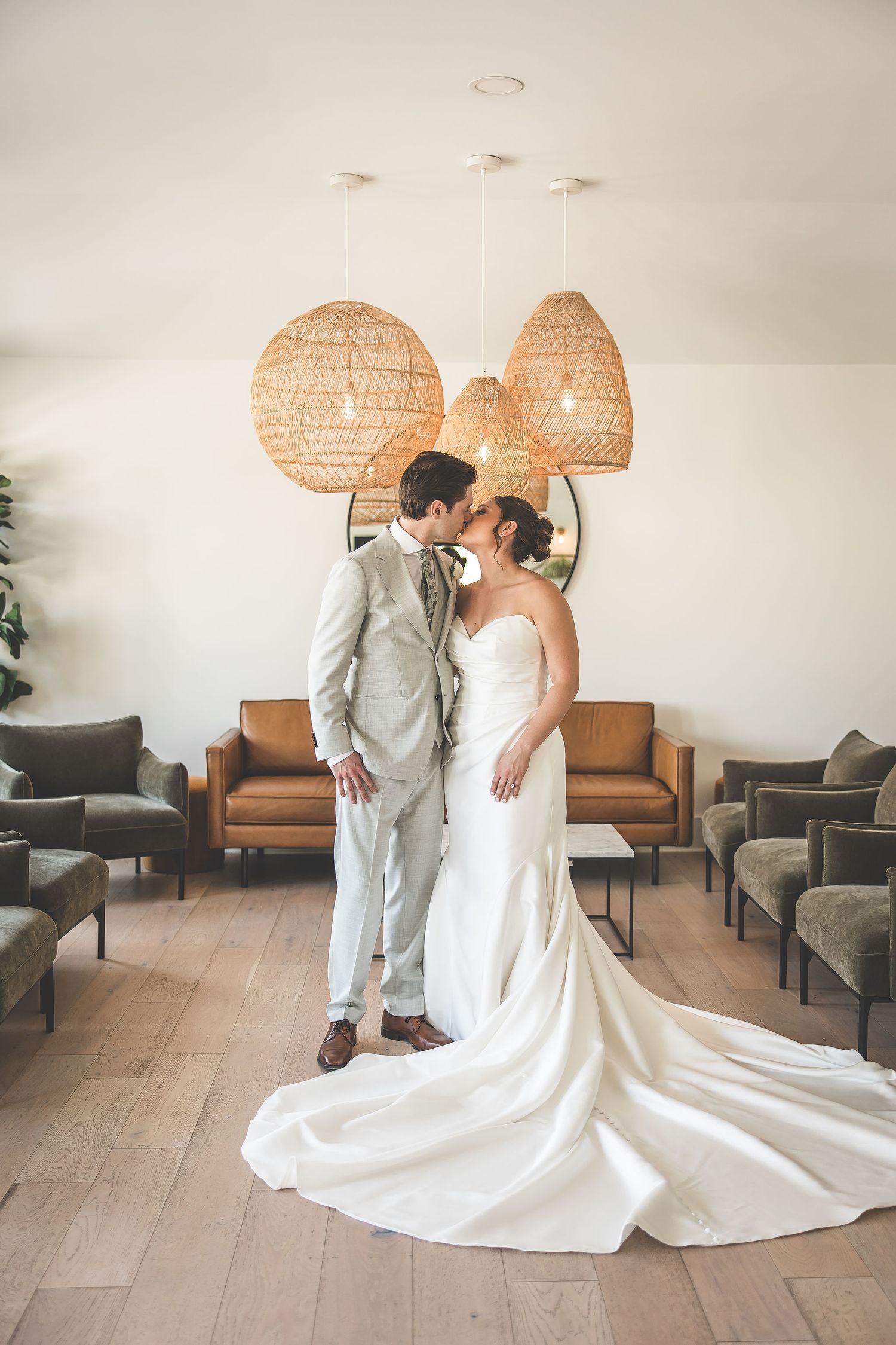 Wedding couple shares intimate moment under woven pendant lights in modern indoor setting.