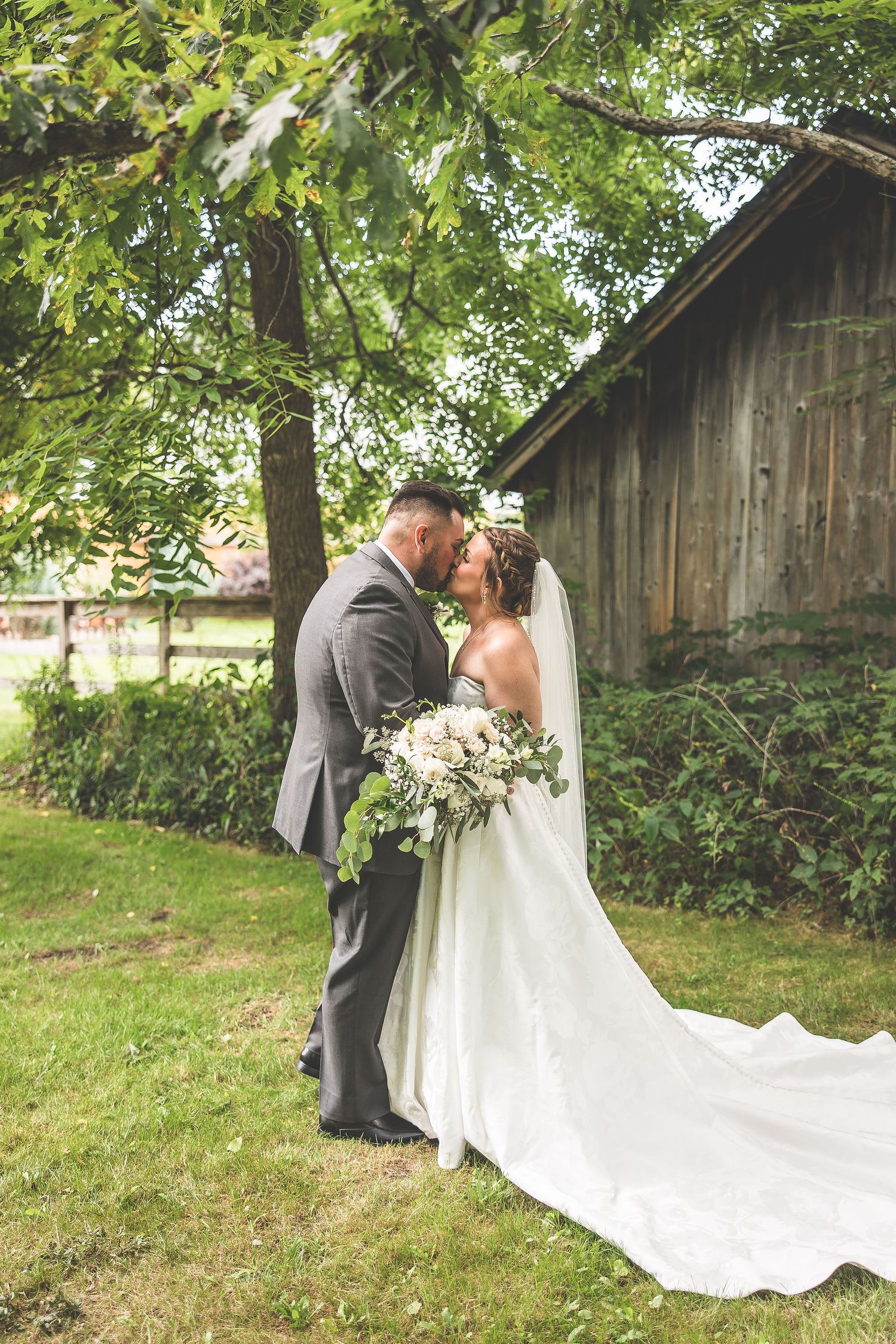 Romantic wedding scene unfolds beside rustic barn with flowing white gown.