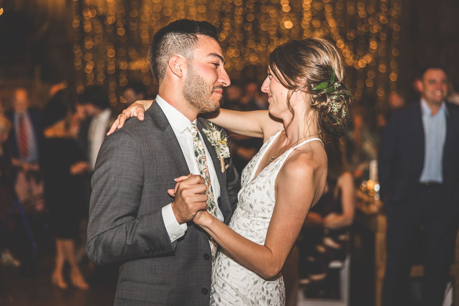 Romantic first dance moment in rustic barn venue with glowing lights.
