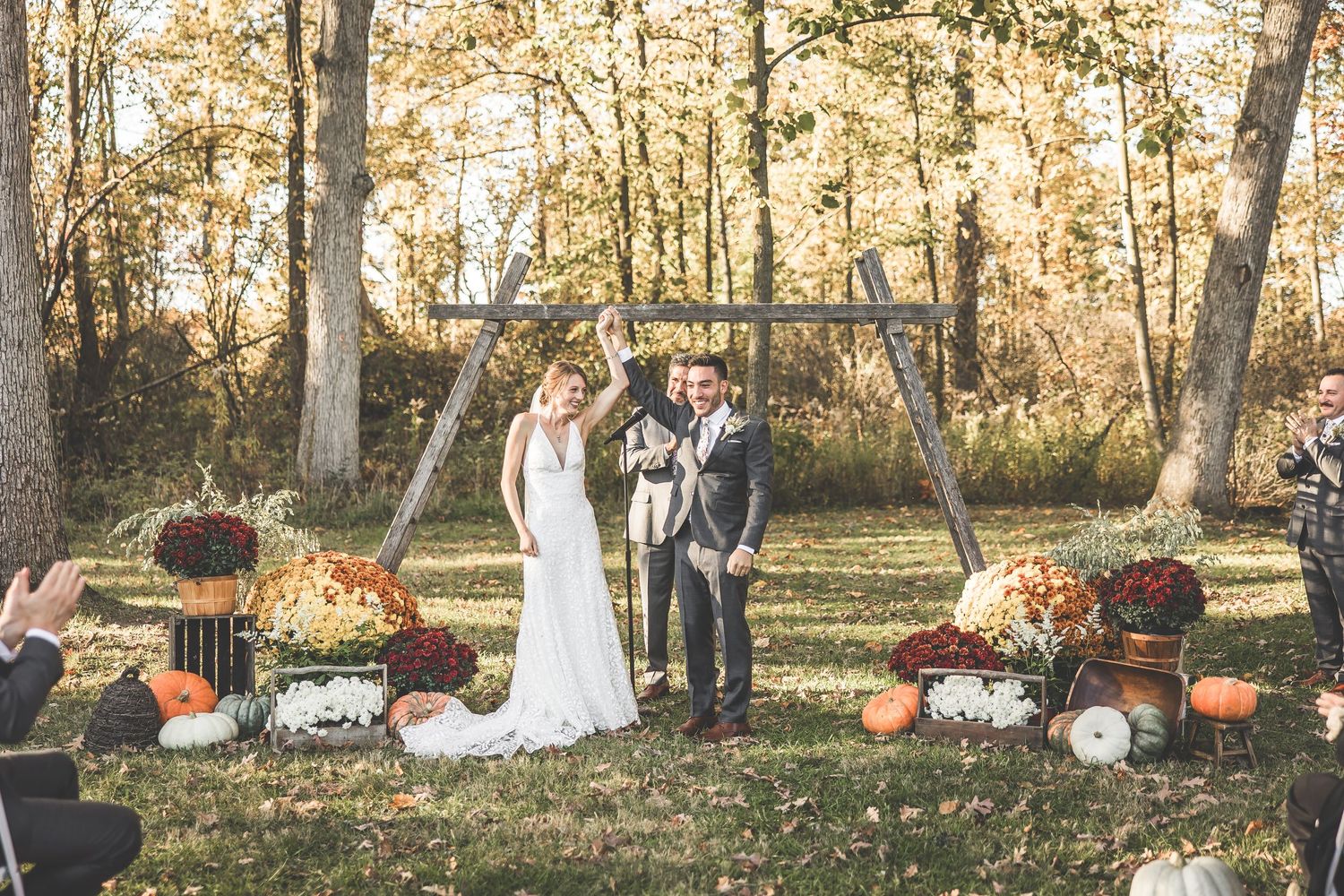 Wedding party poses in an autumn forest setting with pumpkins and fall foliage.