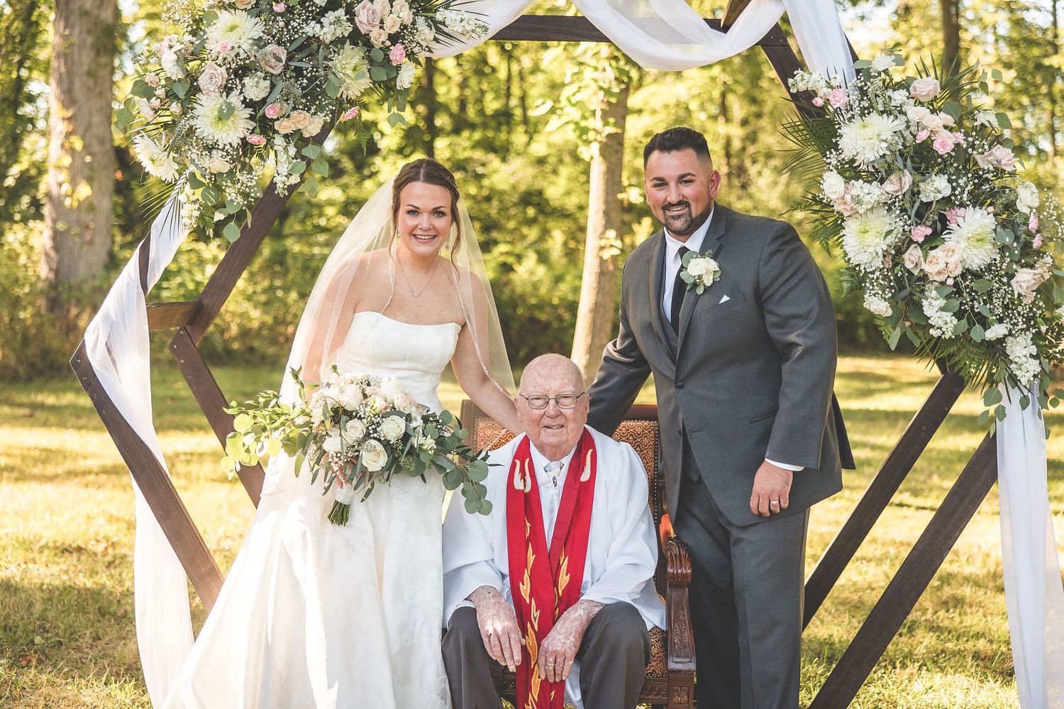 Wedding ceremony under flowering trees with white floral arch and seated guests.