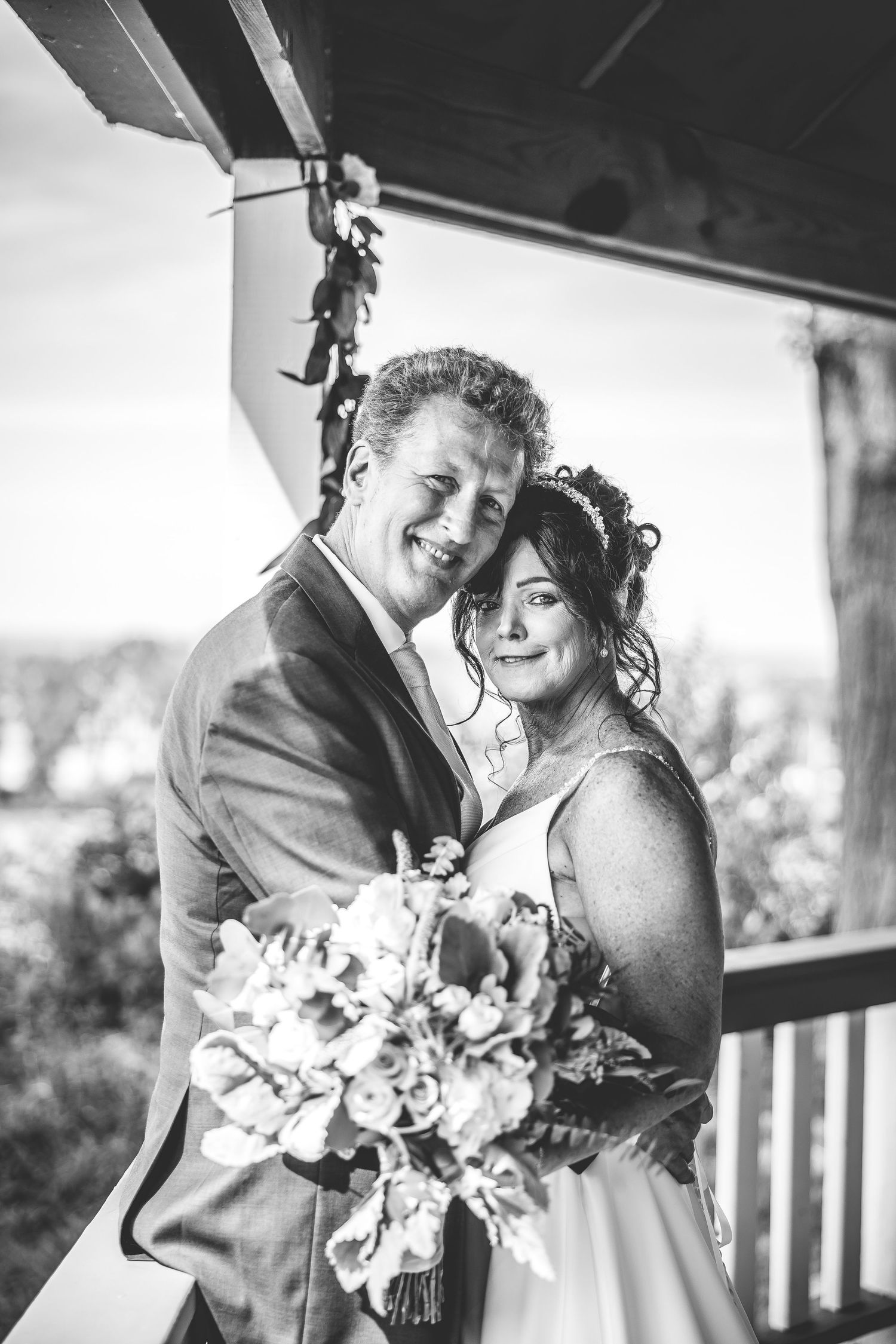 Black and white photo of a couple sharing joyful moments during their wedding on a covered porch.
