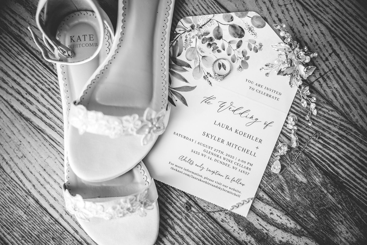 Wedding invitation details and rings arranged on rustic wooden surface.