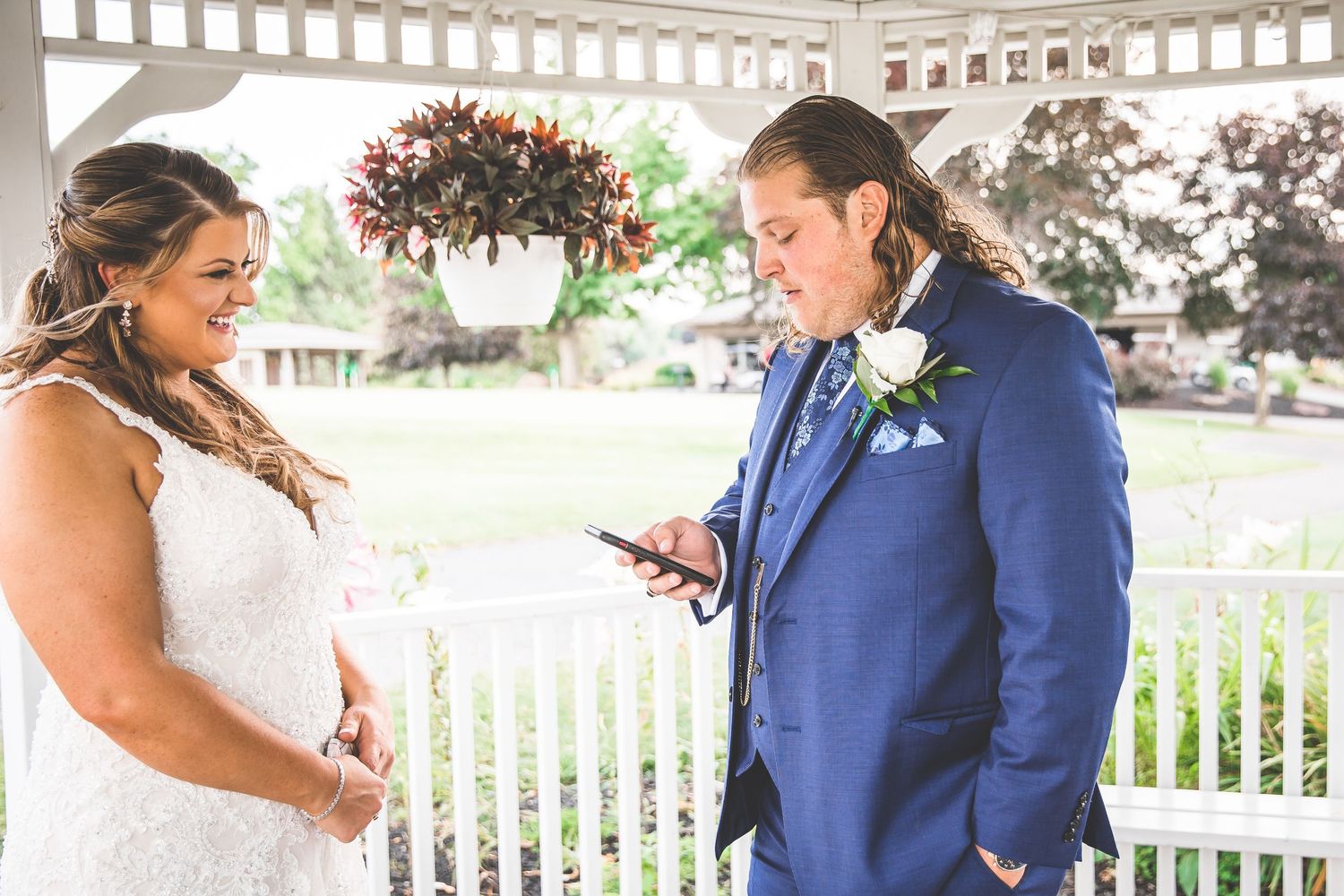 A couple shares a moment while reading vows under a white gazebo during their wedding ceremony.