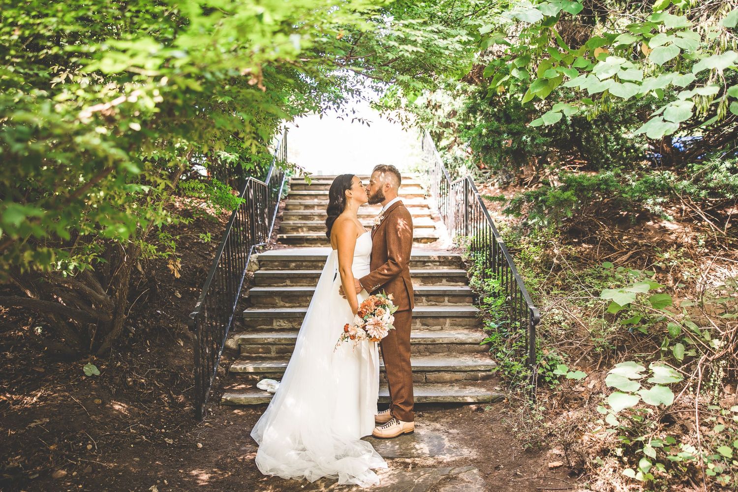 Wedding couple poses on rustic stone steps surrounded by lush forest greenery.