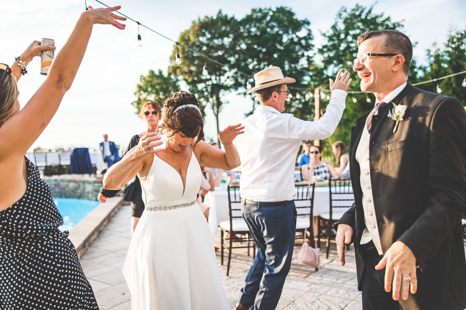 Wedding guests dance and celebrate on an outdoor patio near a pool.