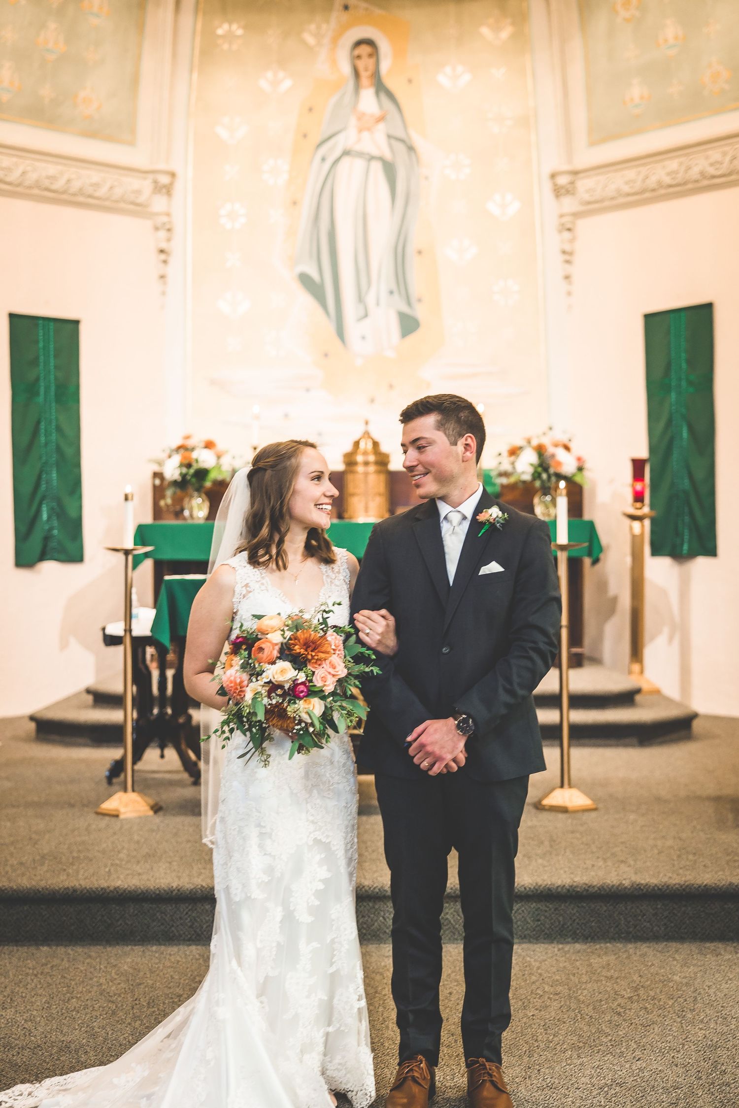 Newlyweds share joyful moments in church sanctuary with decorative green banners and cream walls.