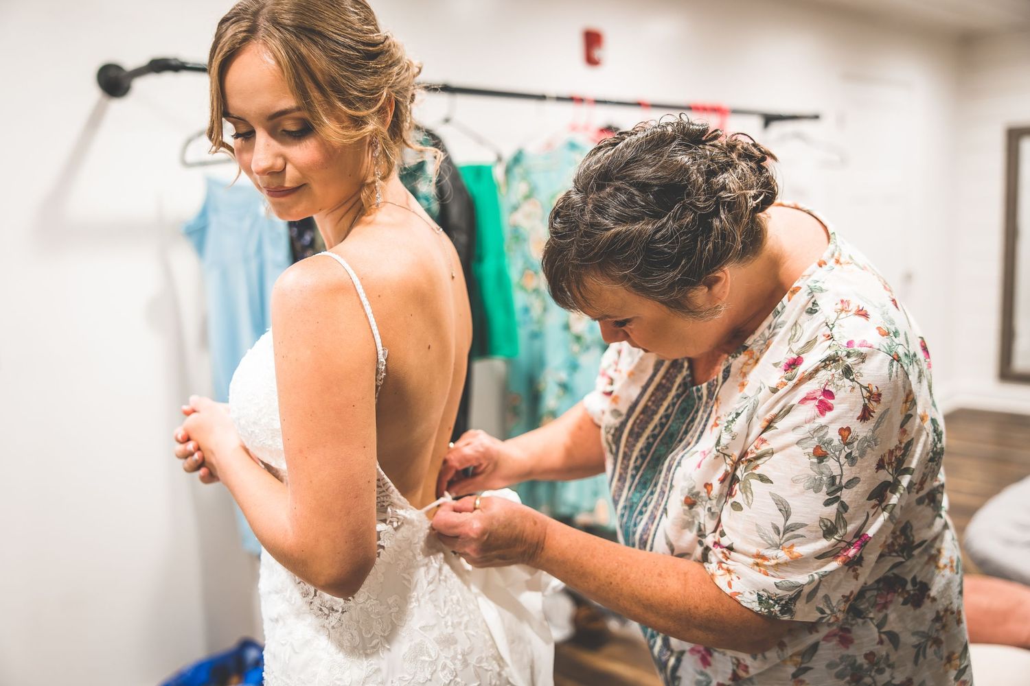 Wedding dress preparation scene with helpers assisting in a bright indoor space.