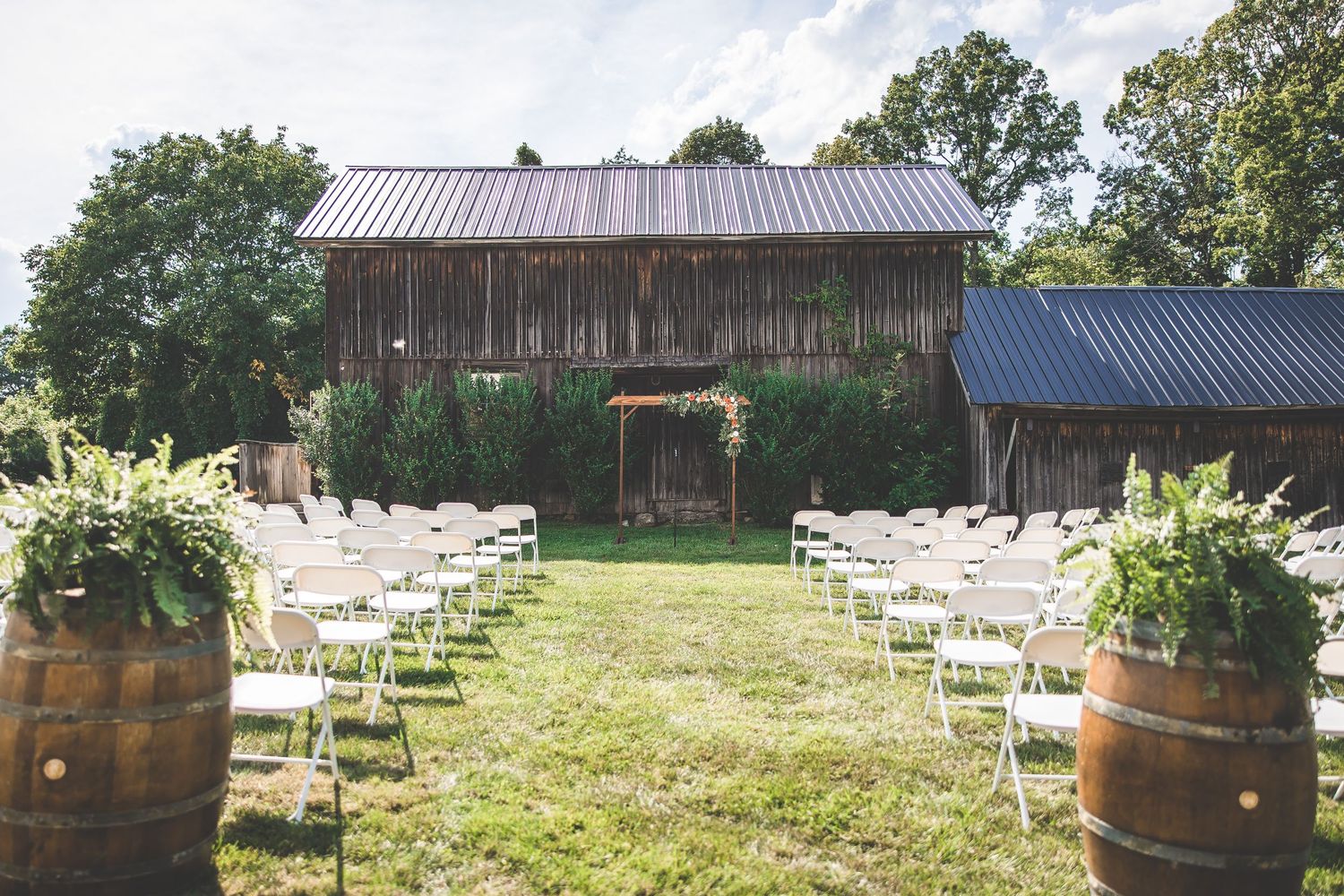 Rustic barn wedding ceremony setup with white chairs and wine barrel decorations.