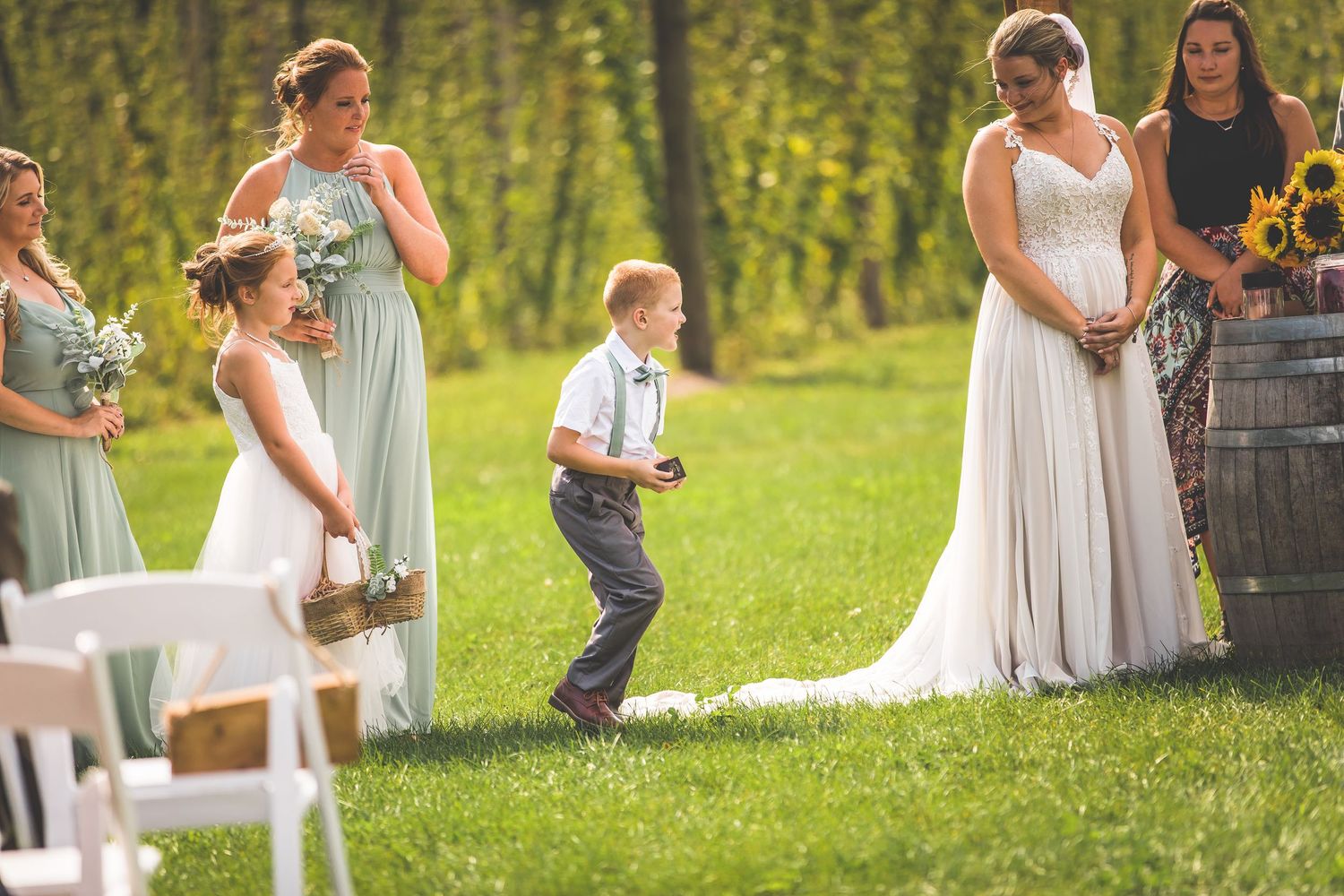 Wedding guests seated on white chairs during outdoor garden ceremony with wooden pergola.