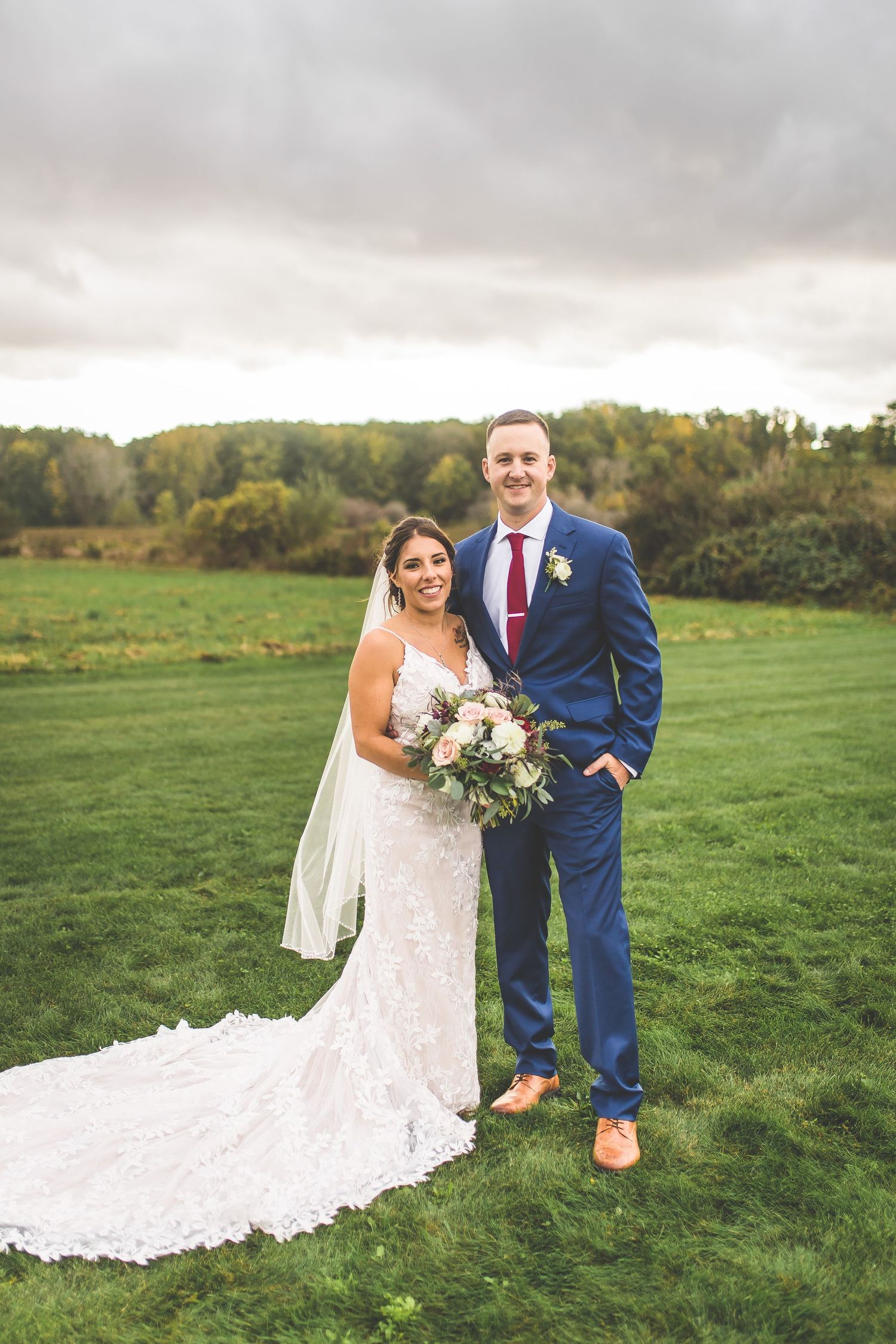 Couple poses playfully in formal attire on a scenic grassy hillside.