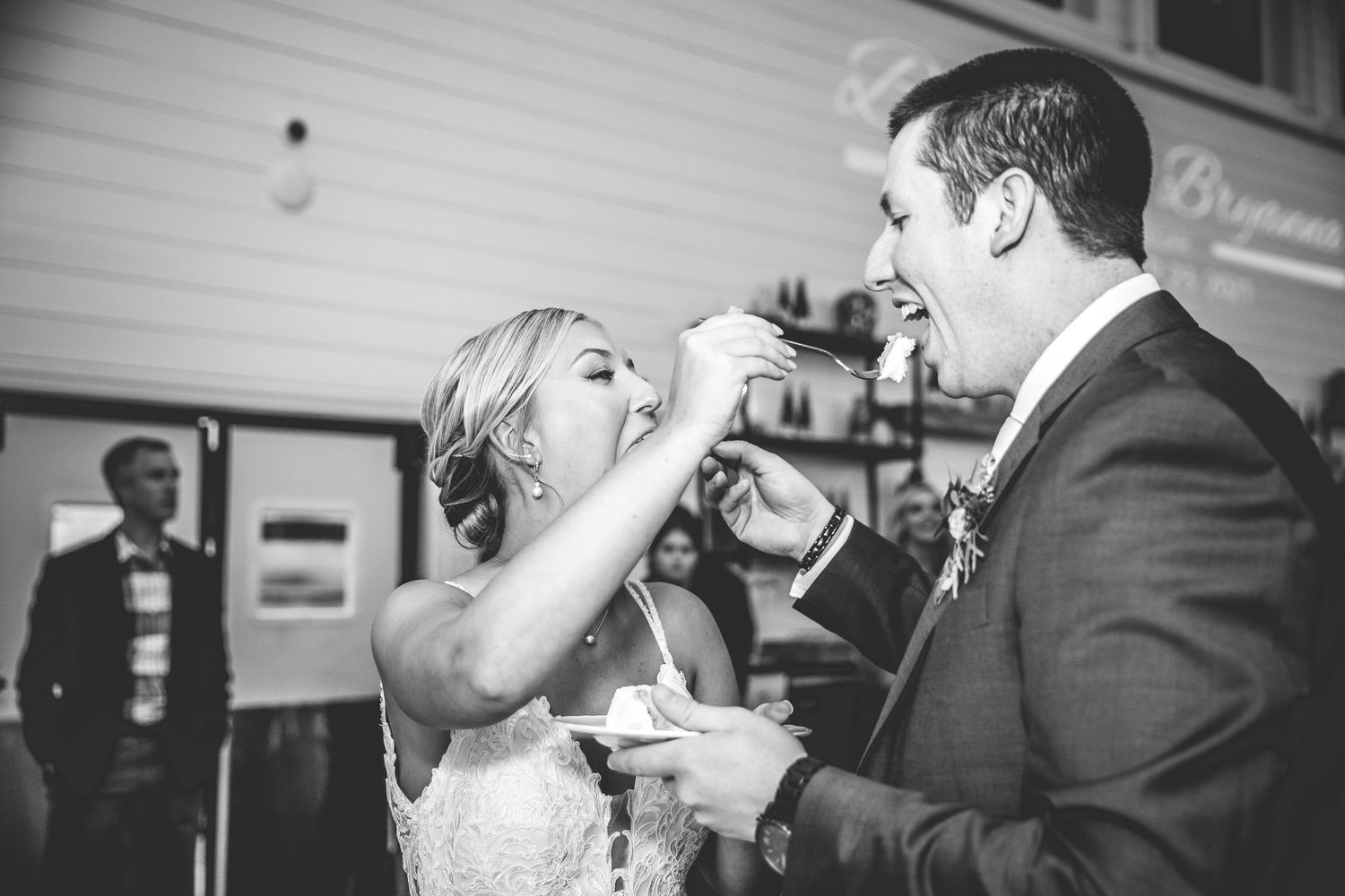 Black and white photo of a couple playfully sharing their wedding cake.