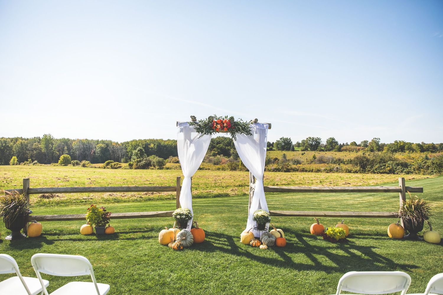 Panoramic view of wedding ceremony site with white arch and chairs on sunny lawn.