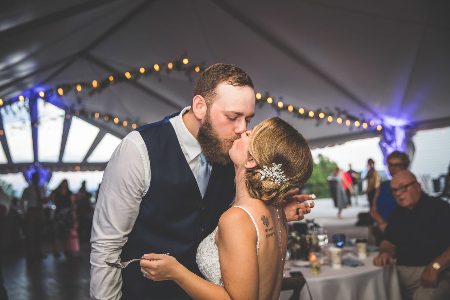 Couples slow dancing under string lights at an evening wedding reception in a tent venue.