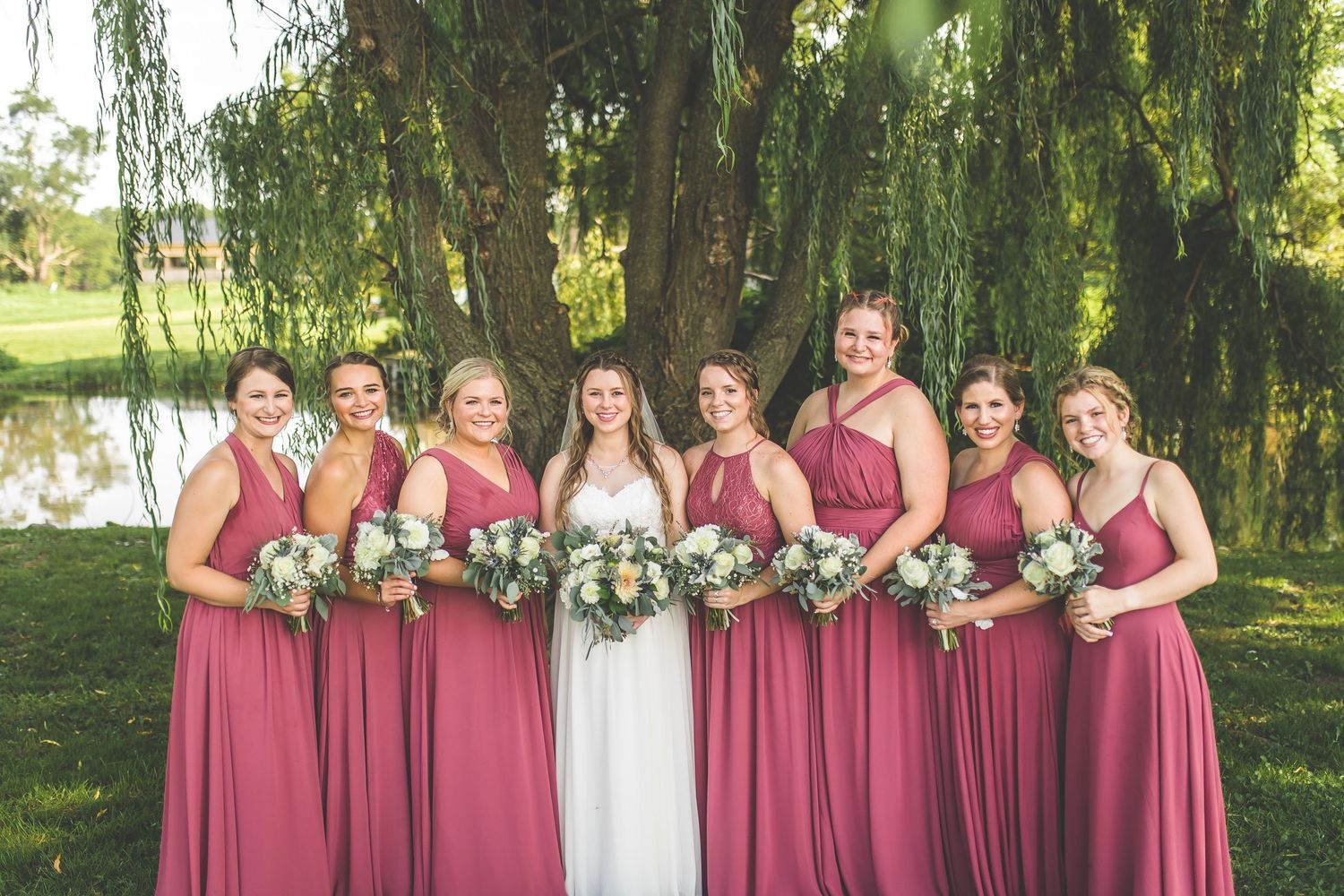 Wedding party lined up under weeping willow trees for formal outdoor photographs.