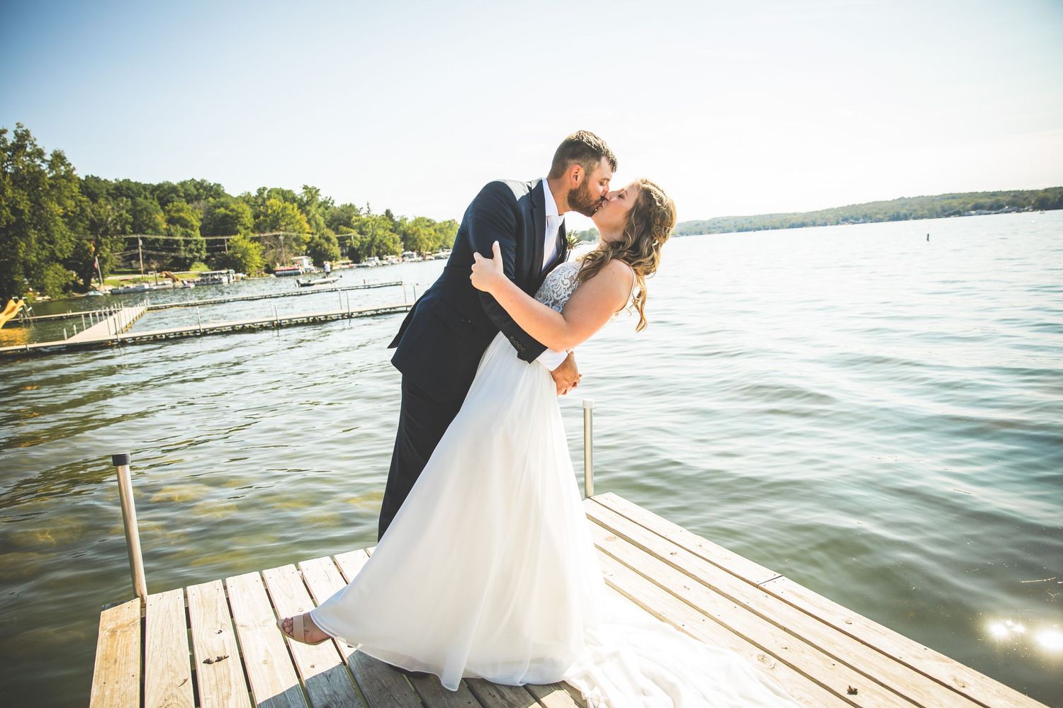A romantic wedding moment captured on a lakeside dock during golden hour.