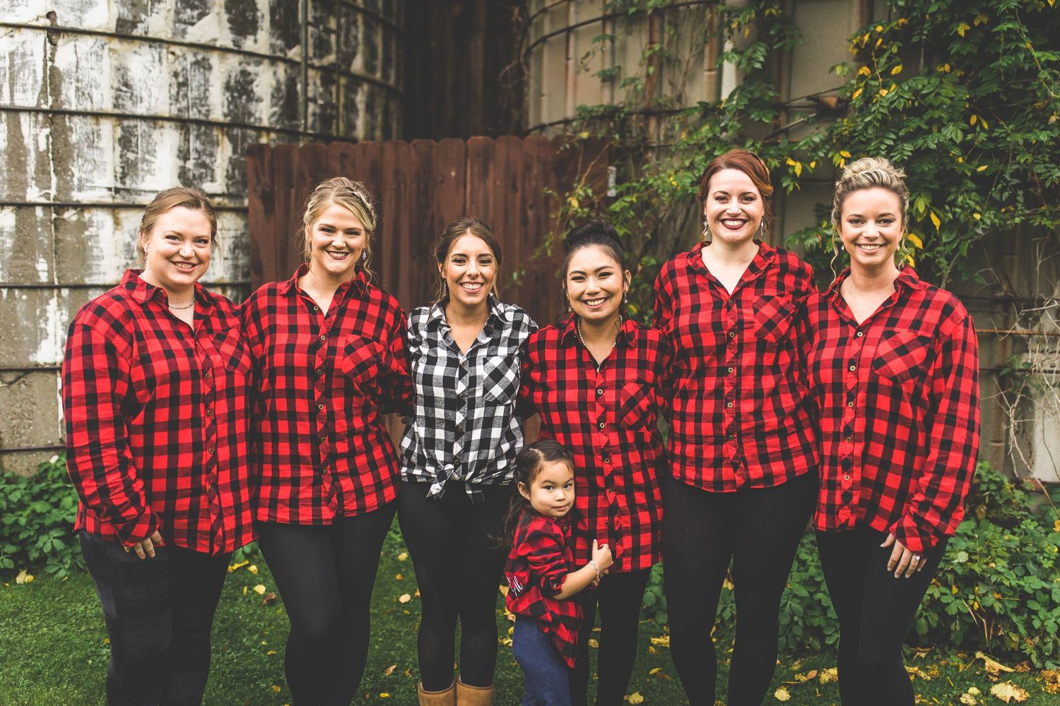 Group photo of people wearing coordinated red and black buffalo plaid shirts outdoors.