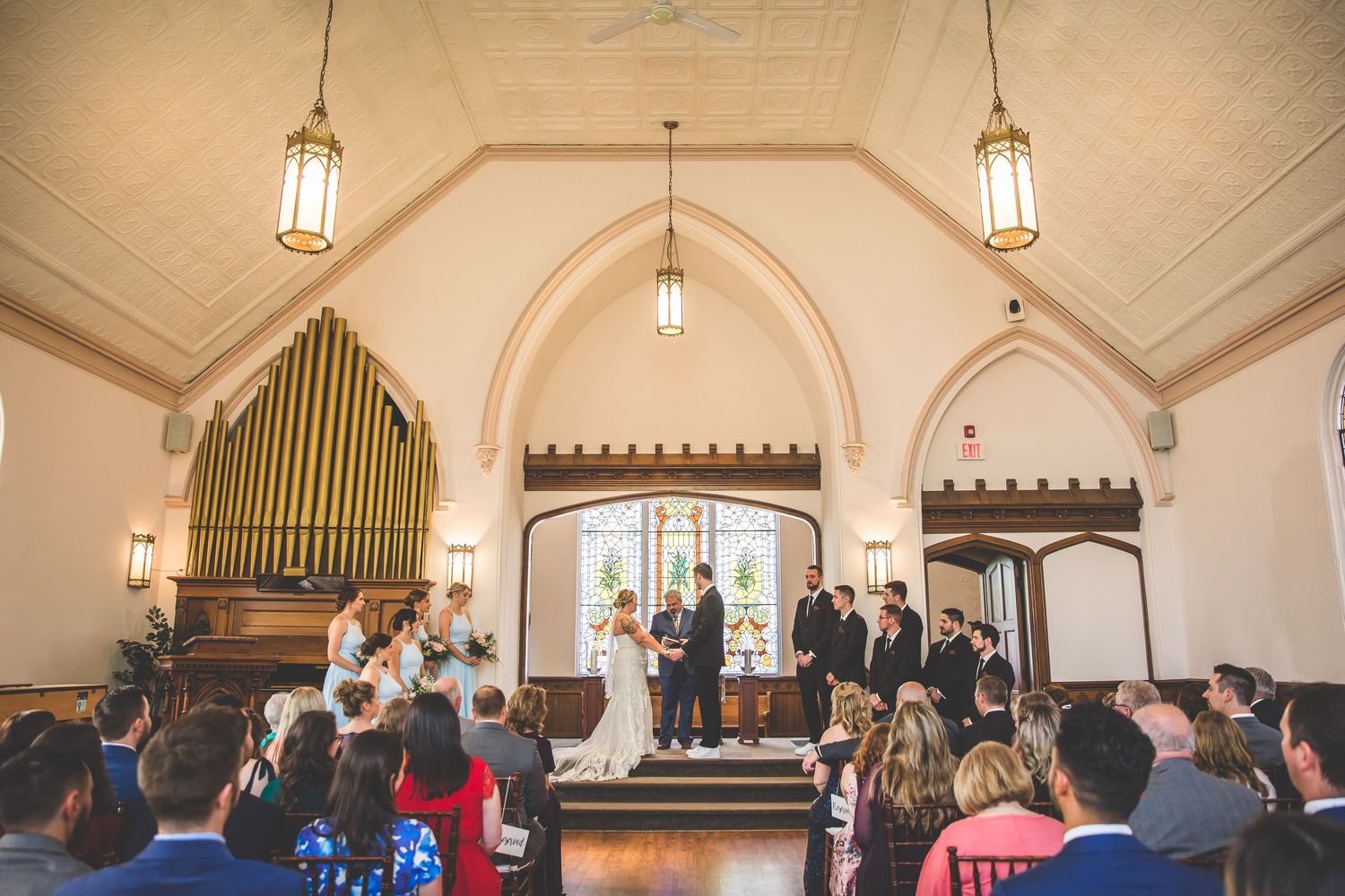 Church interior with hanging lanterns and organ pipes during a wedding ceremony.