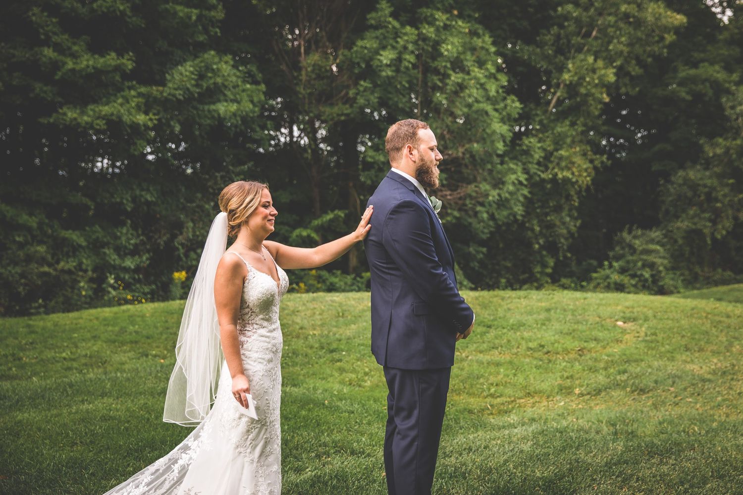 Couple shares tender moment during outdoor wedding first look on grassy hillside.