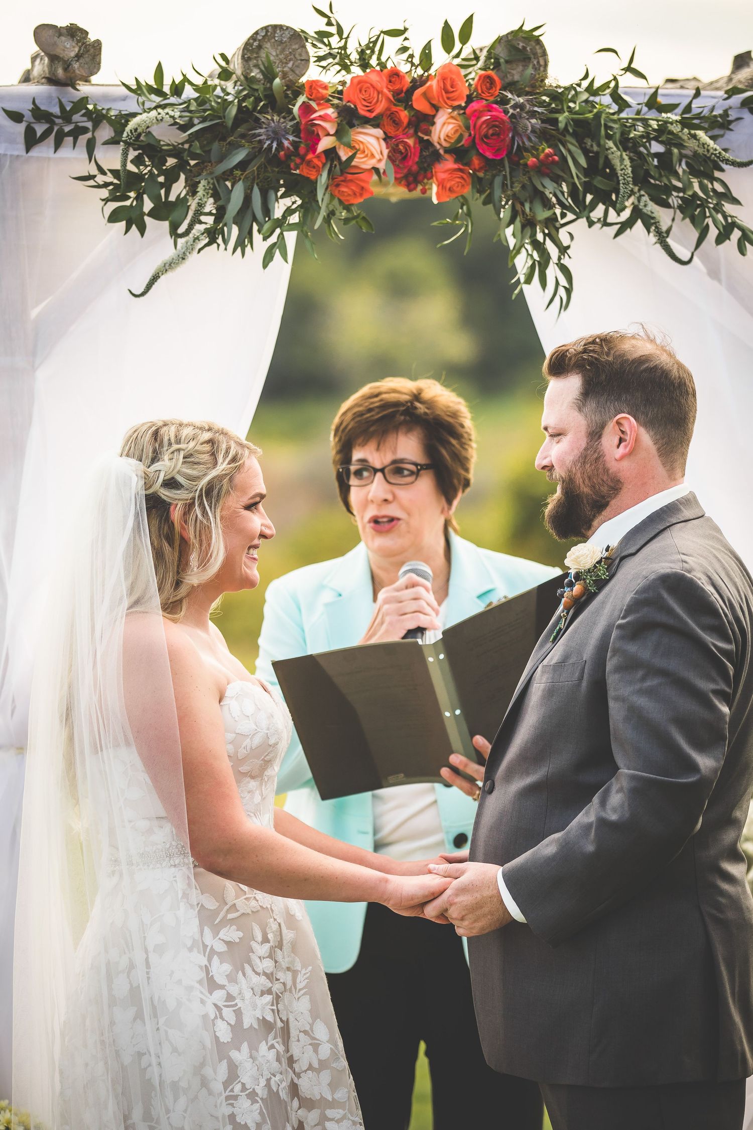 Wedding ceremony under a floral arch with orange and red blooms against a white backdrop.