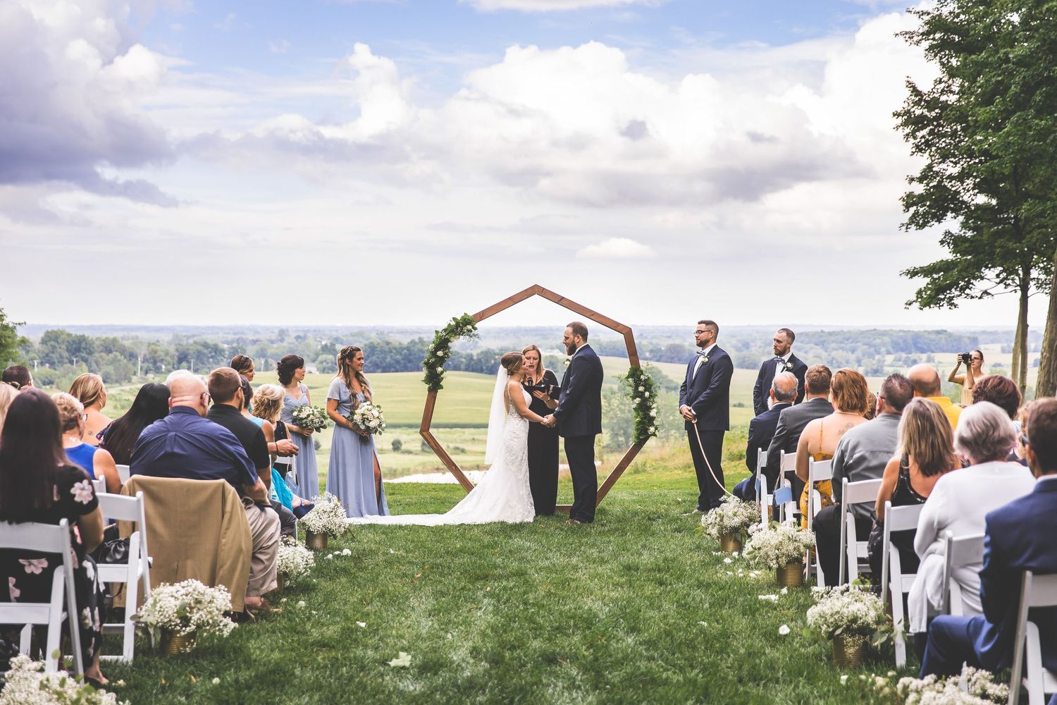 Scenic outdoor wedding ceremony with wooden hexagonal arch and mountain views.