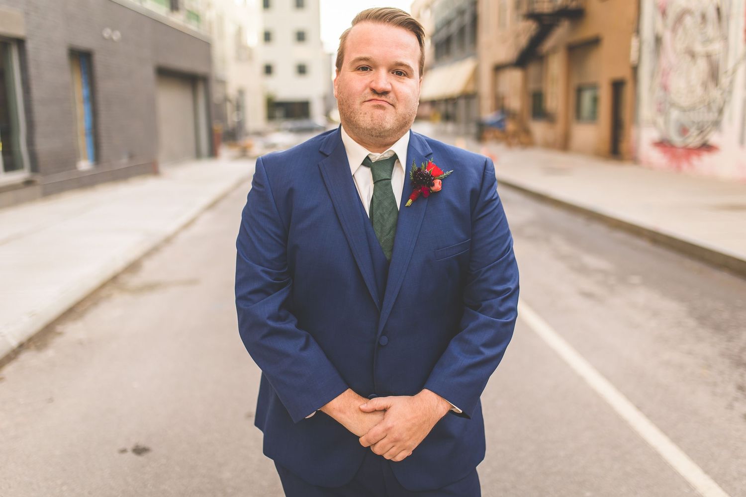 Groom in classic navy suit stands on empty city street during wedding photoshoot.