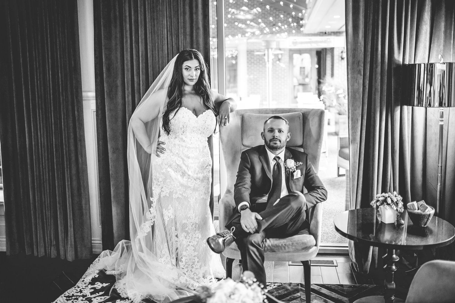 Black and white wedding portrait in luxurious indoor setting with dramatic curtains.