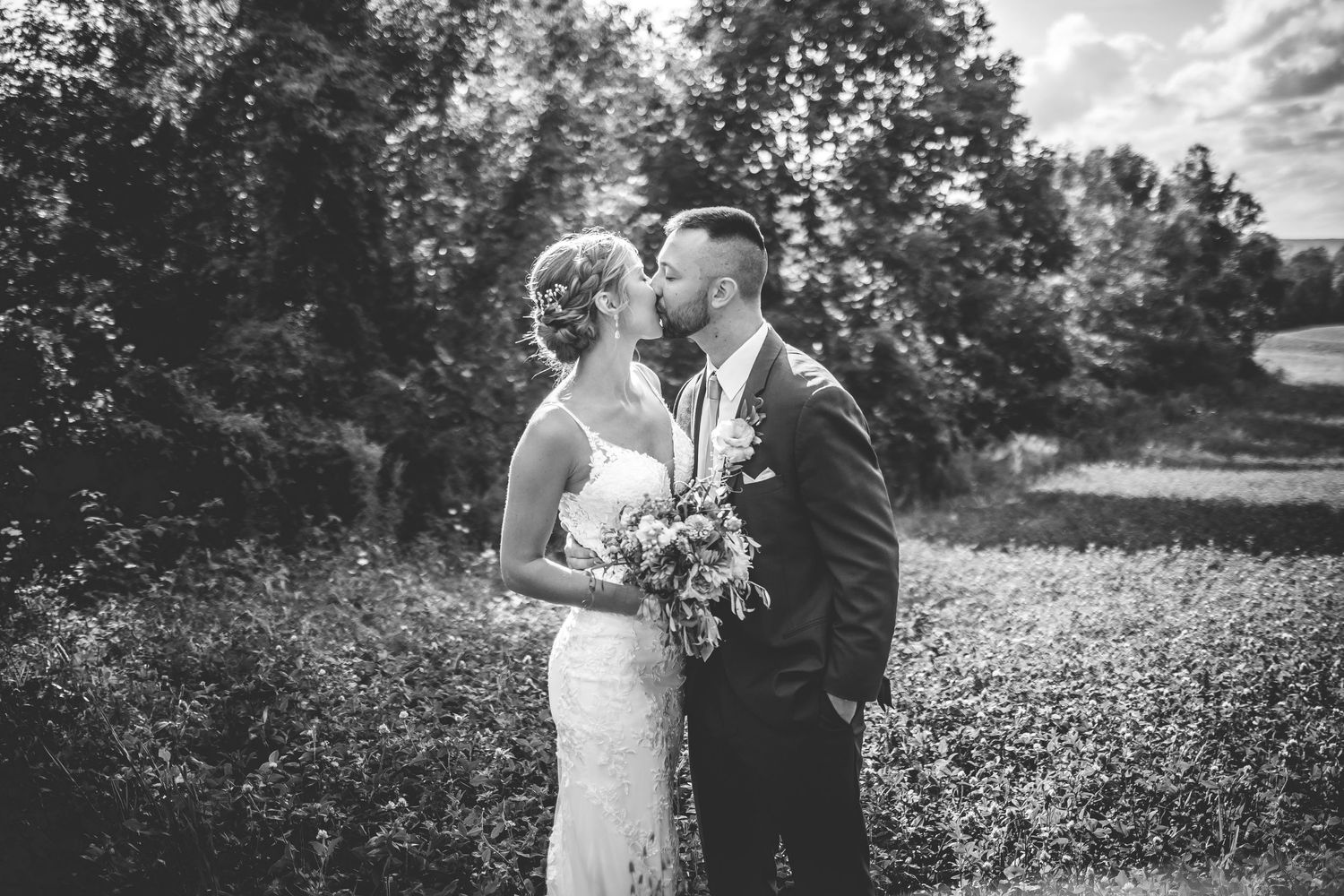 Black and white wedding photos capturing tender moments between newlyweds in a rural landscape.