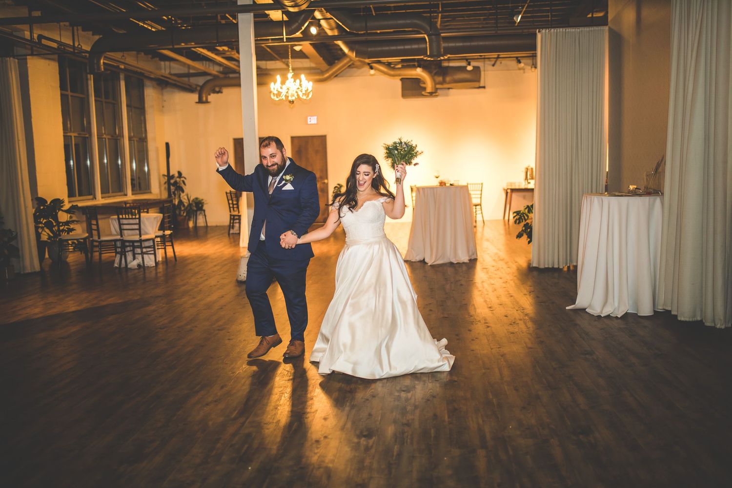 Couple shares their first dance in a beautifully decorated reception hall with string lights overhead.