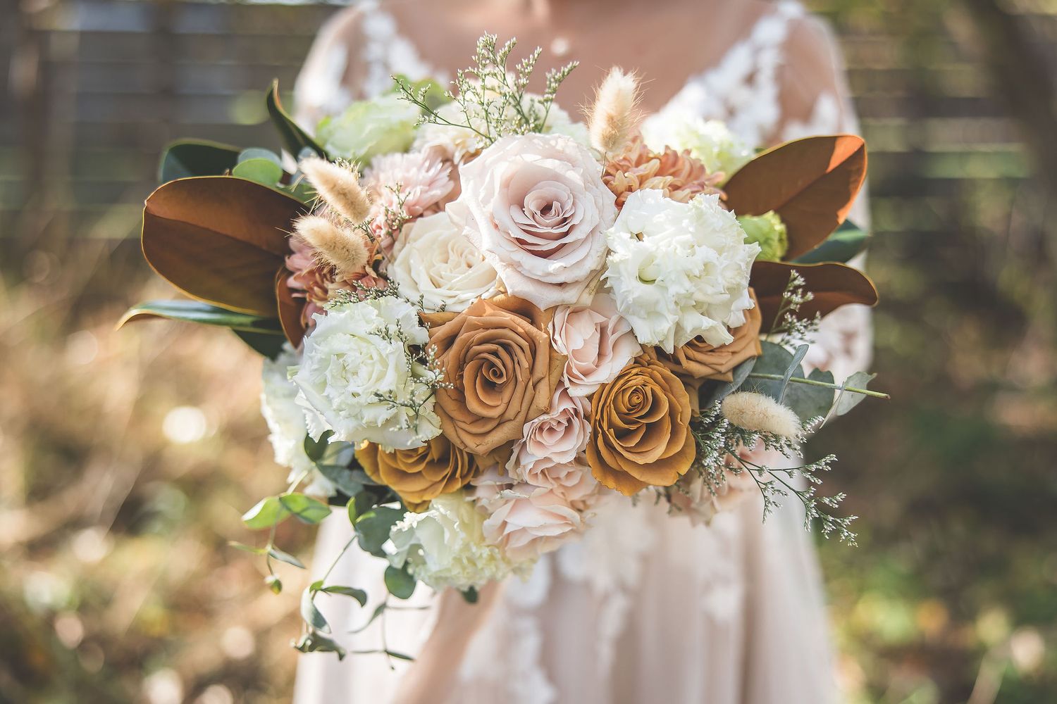 Delicate pink and white floral wedding bouquet with roses and greenery against a natural outdoor backdrop.
