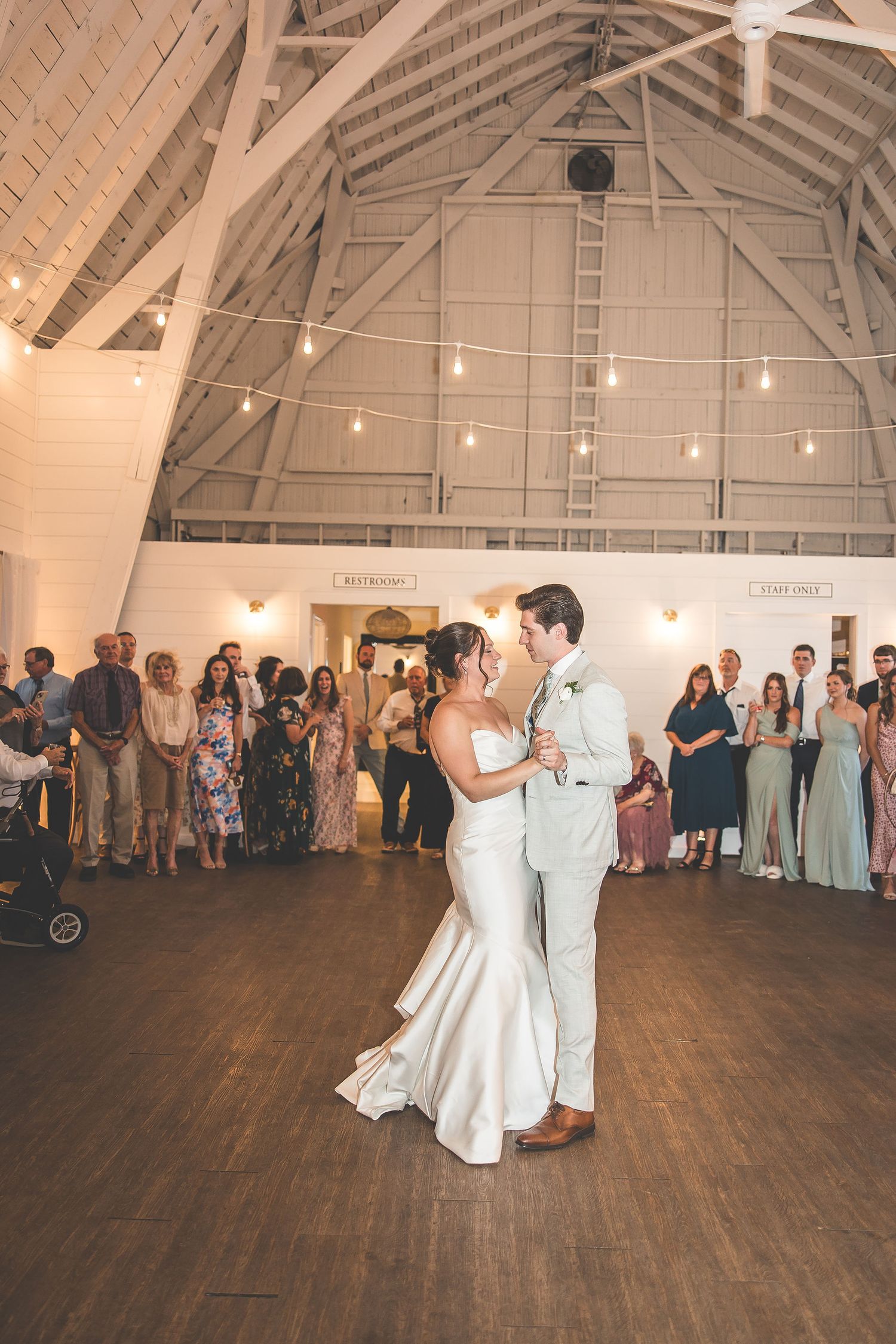 Couples share romantic dances on a wooden floor in a barn-style venue with string lights.
