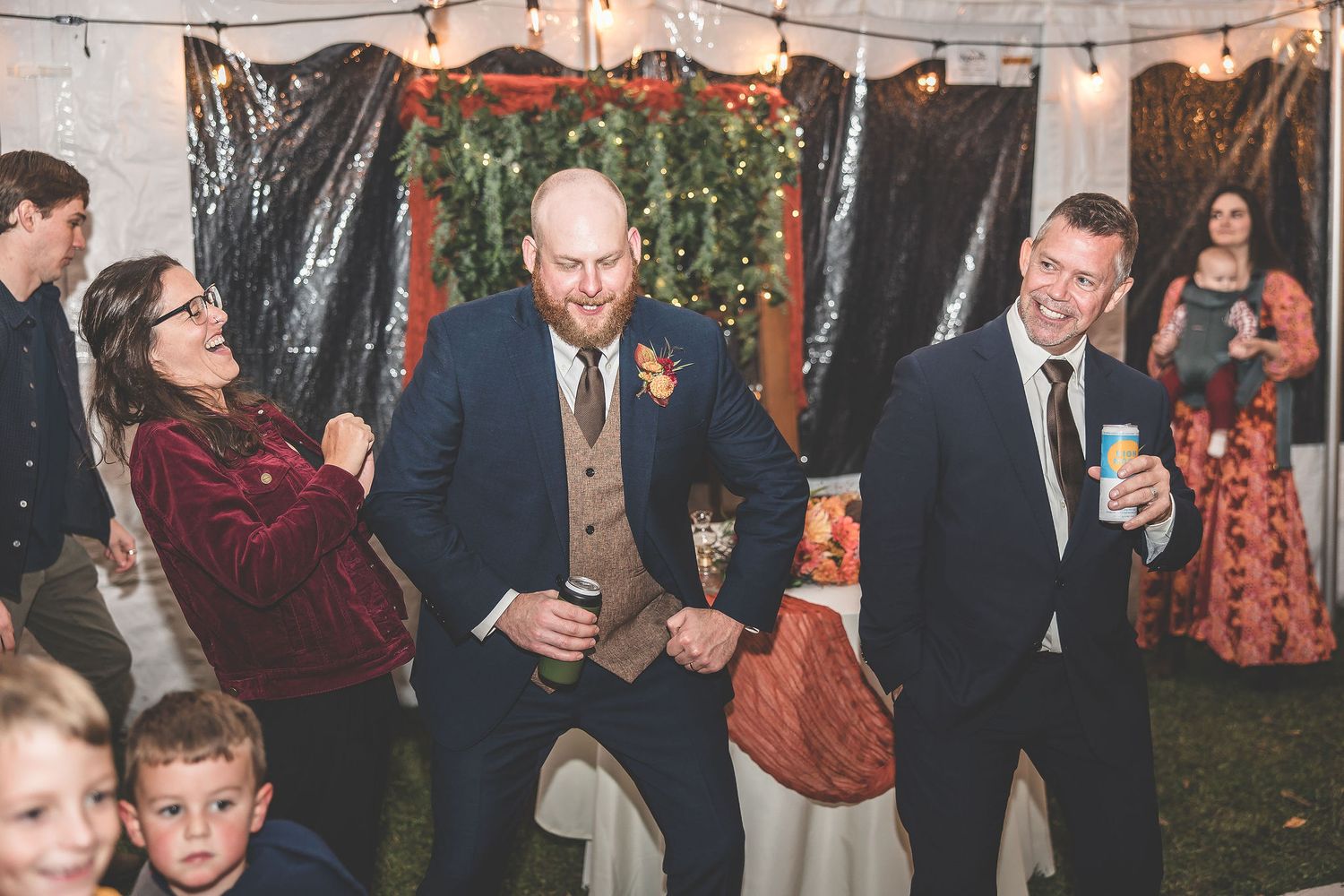 Wedding reception guests dancing and mingling under string lights in an indoor-outdoor venue.