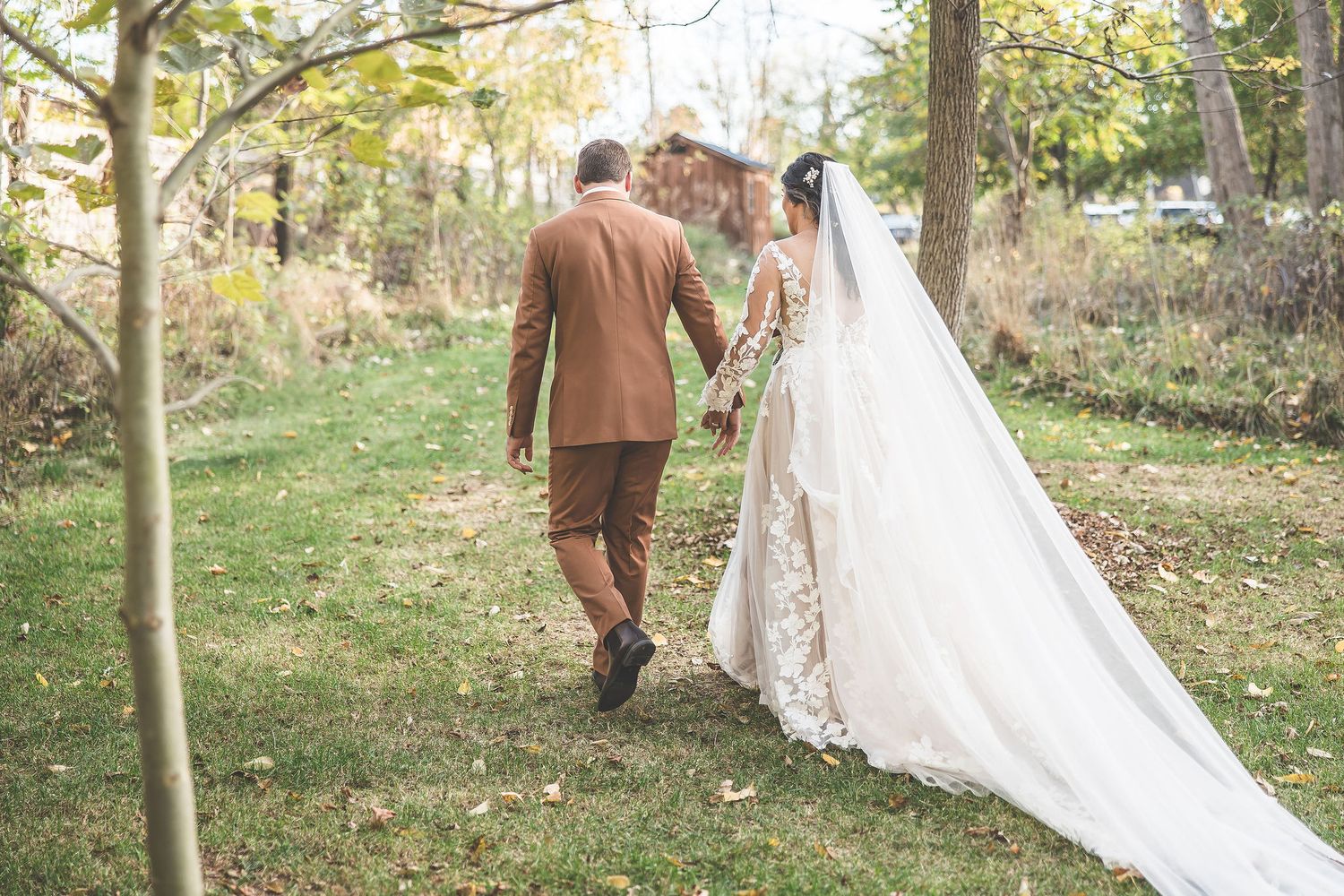 Newlyweds walking through wooded outdoor ceremony space with natural fall scenery.