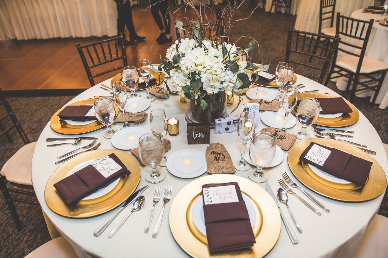 Elegant wedding reception table settings with gold chargers and burgundy napkins.