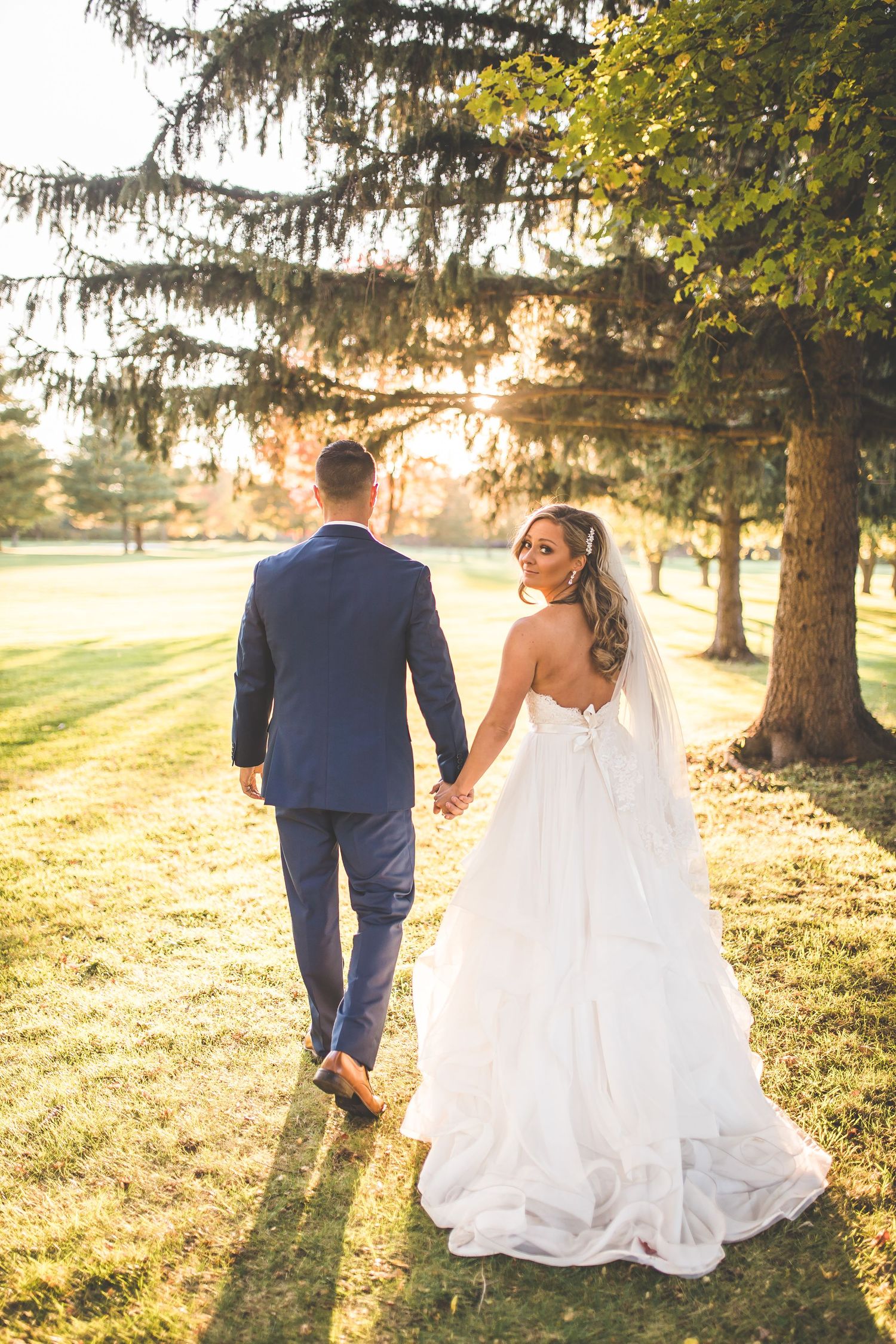 Romantic sunset wedding photos in a field with golden light filtering through trees.