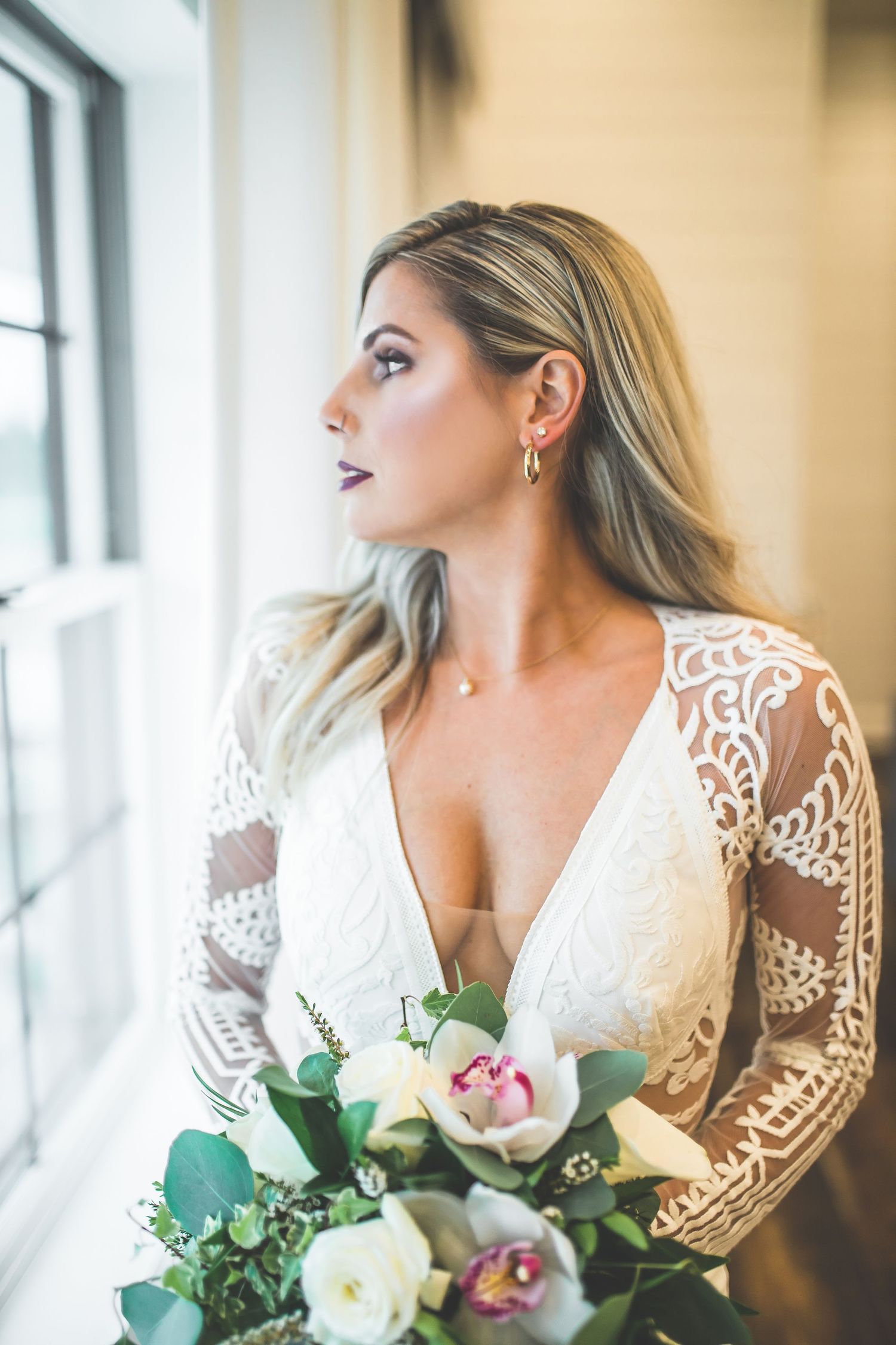 Elegant bridal portrait by a window featuring lace dress details and white floral bouquet.