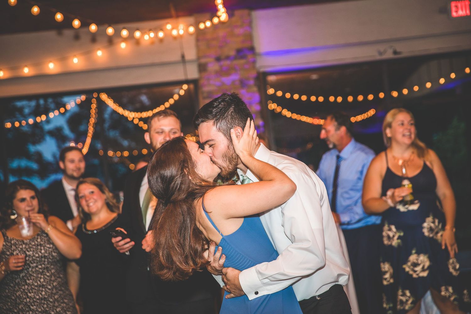Couple shares a romantic dance moment under string lights at their wedding reception.