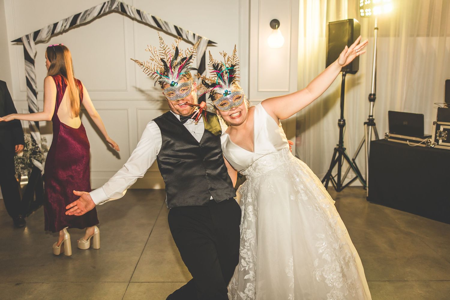 Wedding guests dancing and celebrating in a white-walled reception venue with festive lighting.