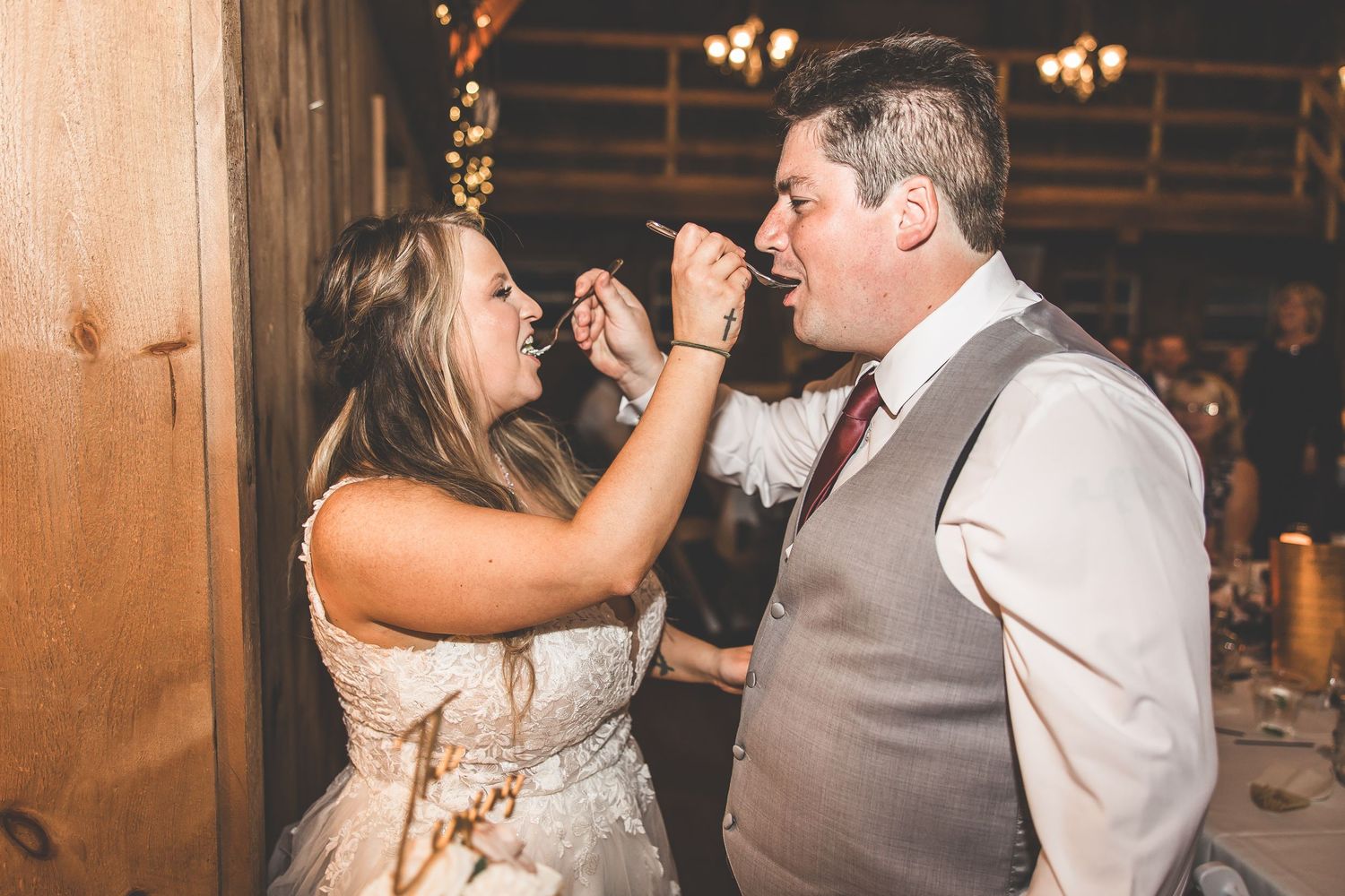 Wedding guests dancing and celebrating on a rustic wooden dance floor with string lights overhead.