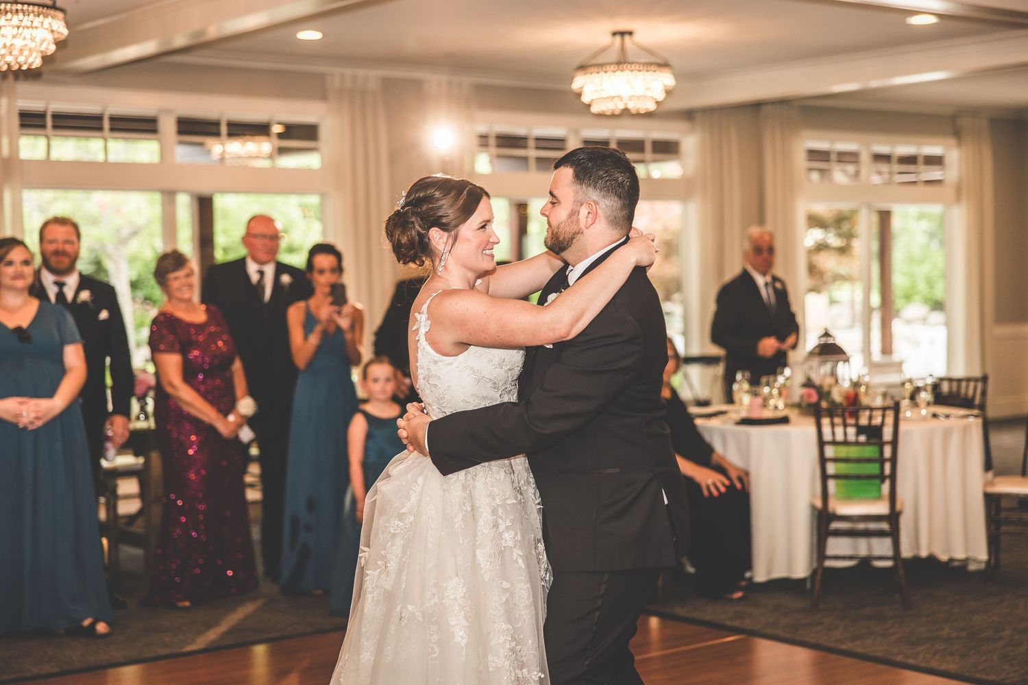 Wedding celebration in a bright ballroom with guests dancing under crystal chandeliers.