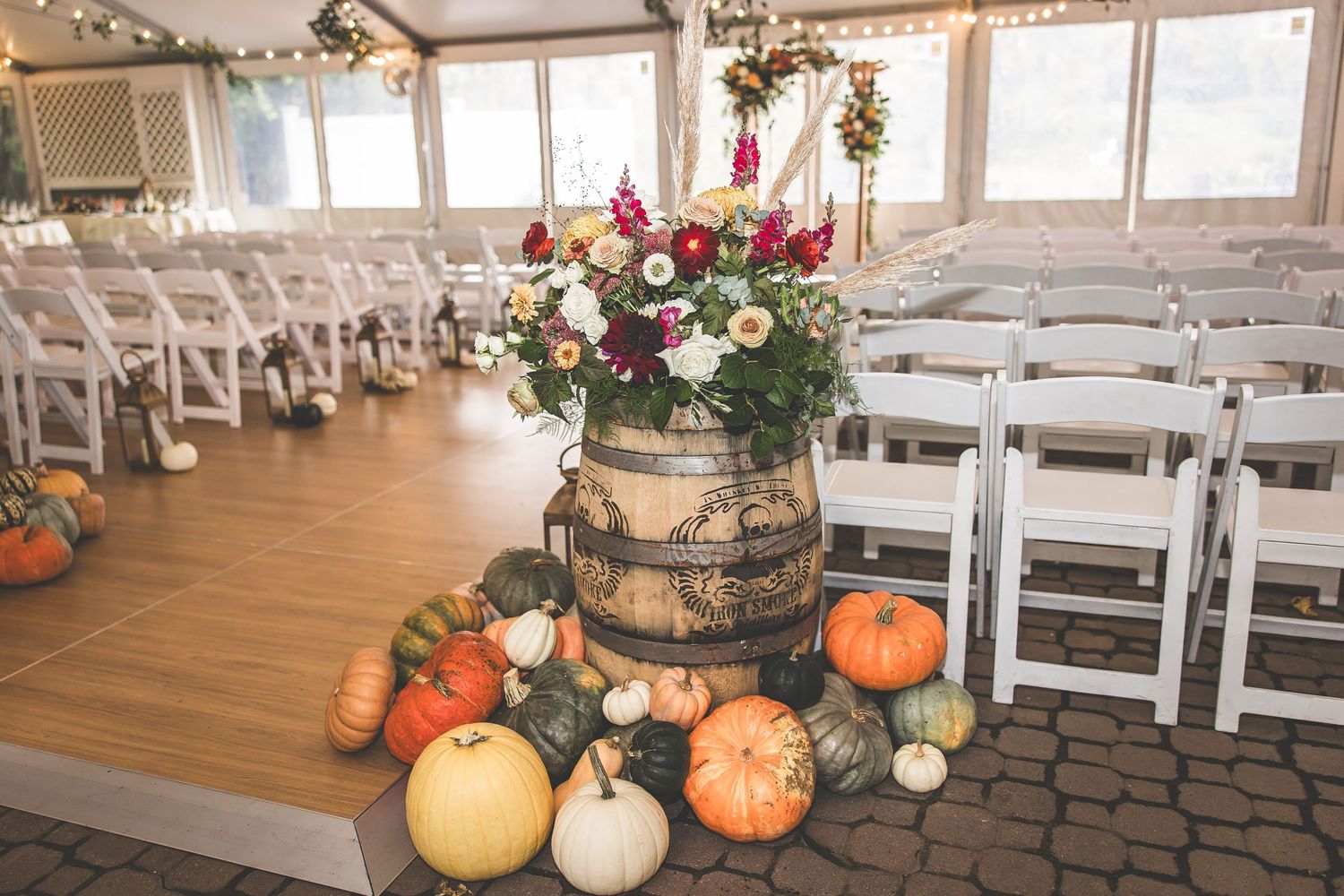 Wedding venue interior decorated with string lights, white chairs and autumn pumpkins.