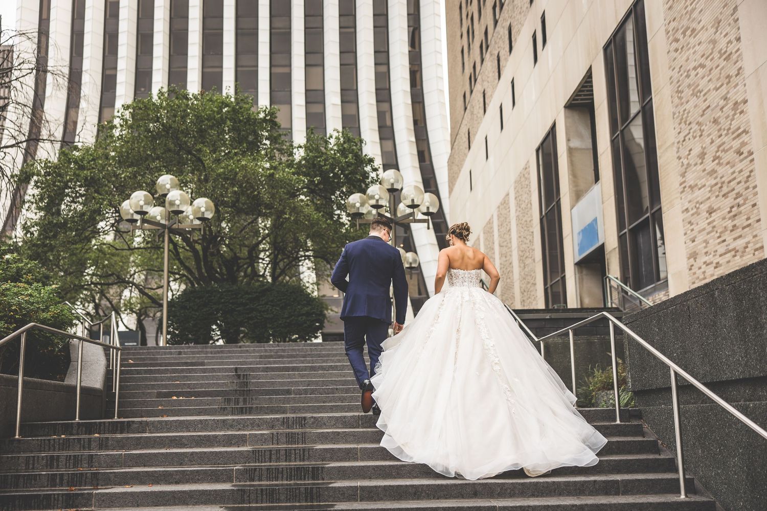 Couple ascending urban stone steps with dramatic wedding dress trailing behind.