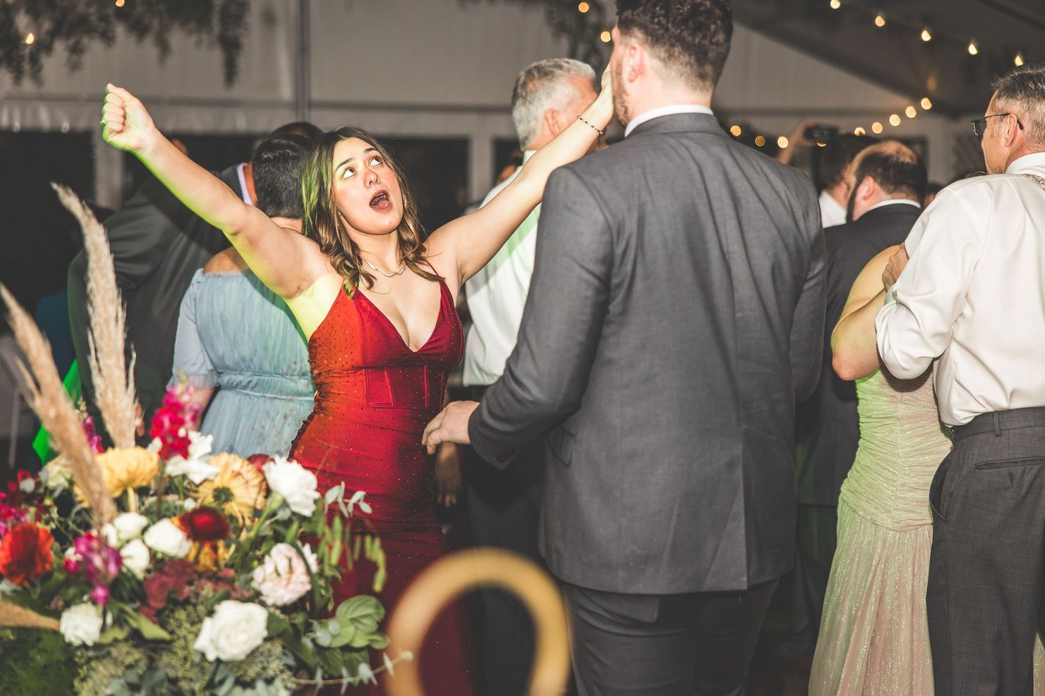 Wedding party dancing and celebrating with arms raised under twinkling lights.