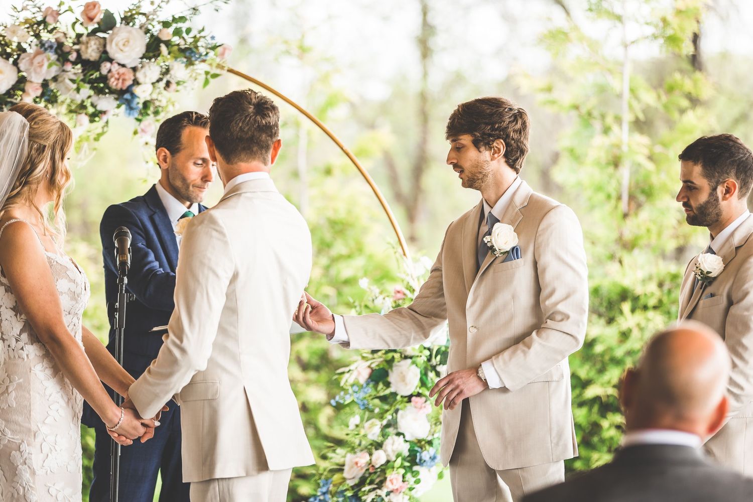 Wedding ceremony participants gather around couple during vow exchange.